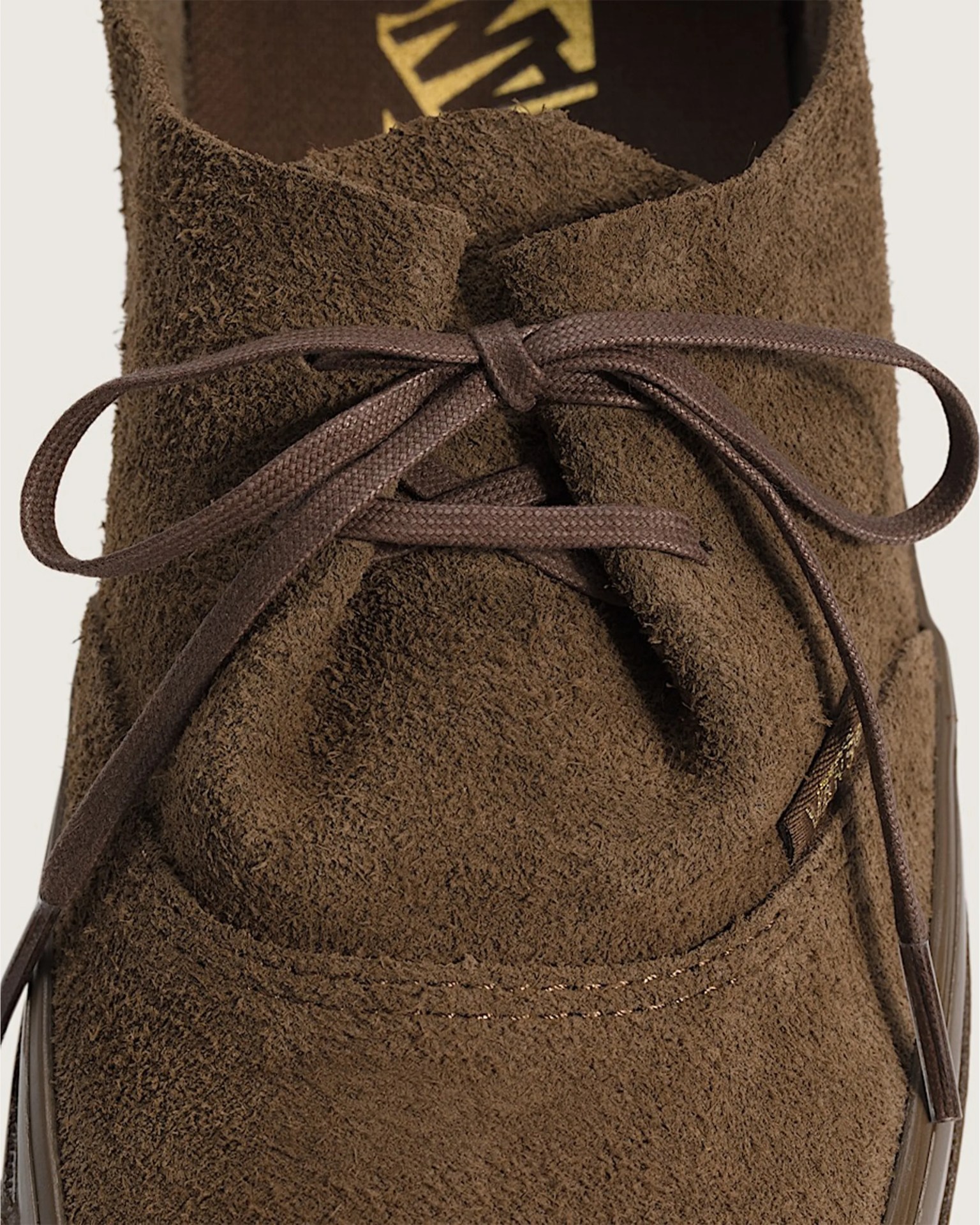 Close-up of a brown suede shoe with matching brown laces tied in a bow.