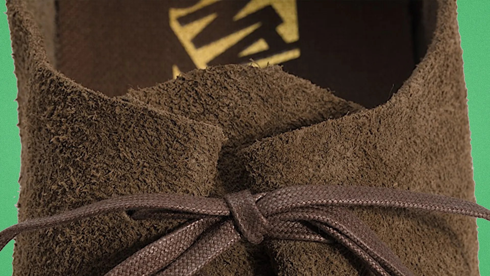 Close-up of brown suede shoe with brown laces tied in a bow against a green background.
