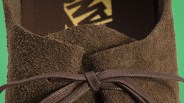 Close-up of brown suede shoe with brown laces tied in a bow against a green background.