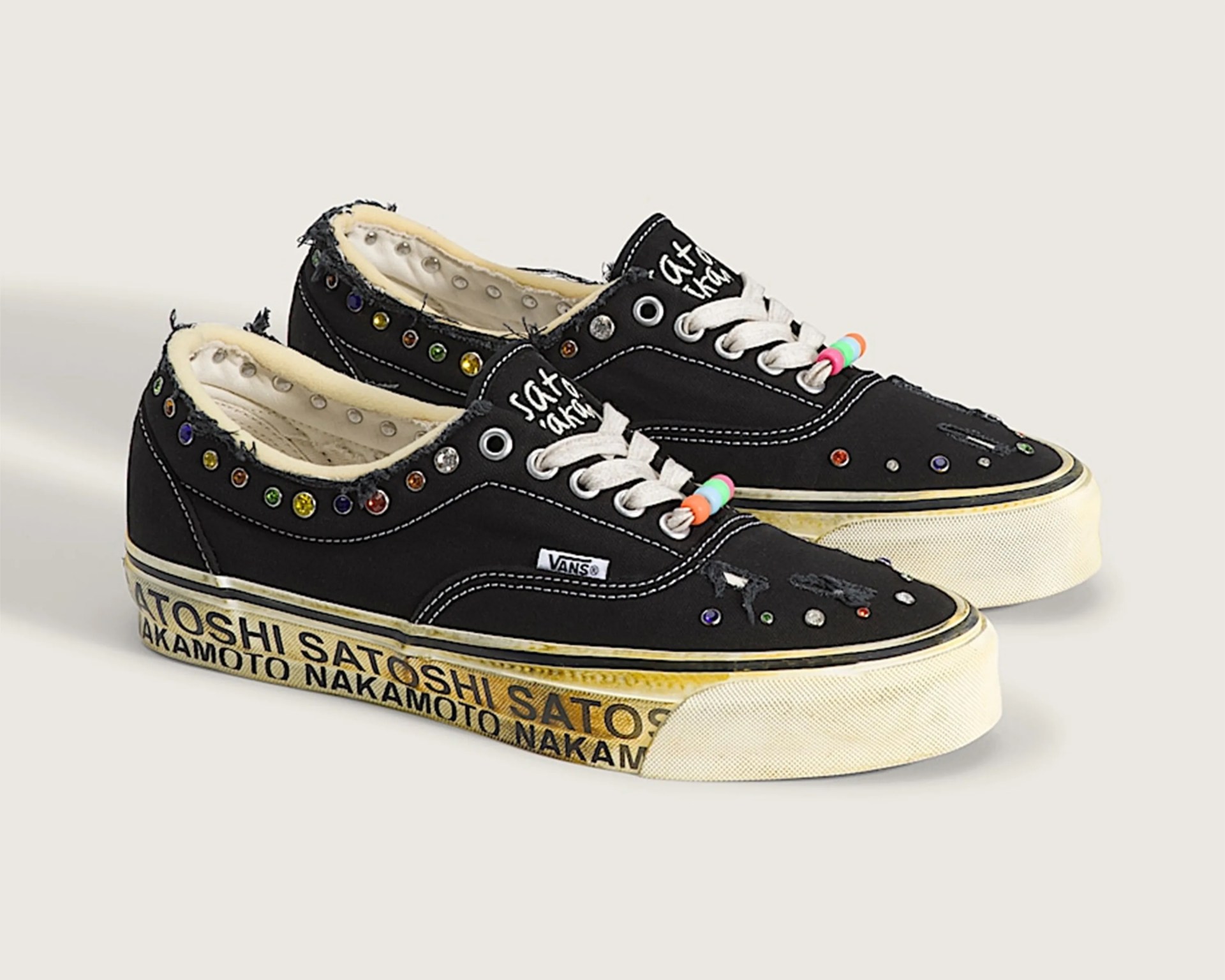 Black Vans sneakers with white laces, multicolored rhinestones, frayed edges, and "Satoshi Nakamoto" text on the sole.