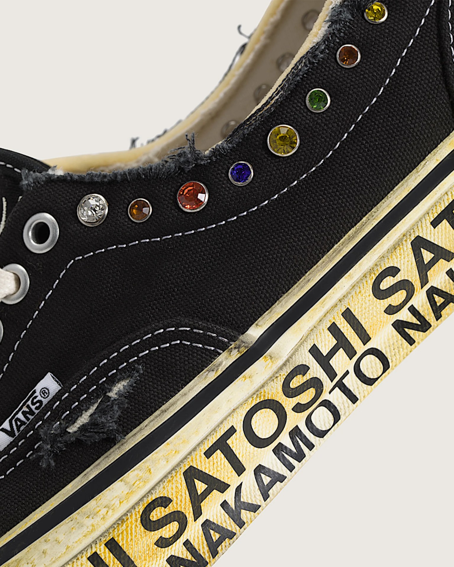 Black Vans sneaker with frayed edges, multicolored rhinestones on the upper, and yellowed sole with black text.