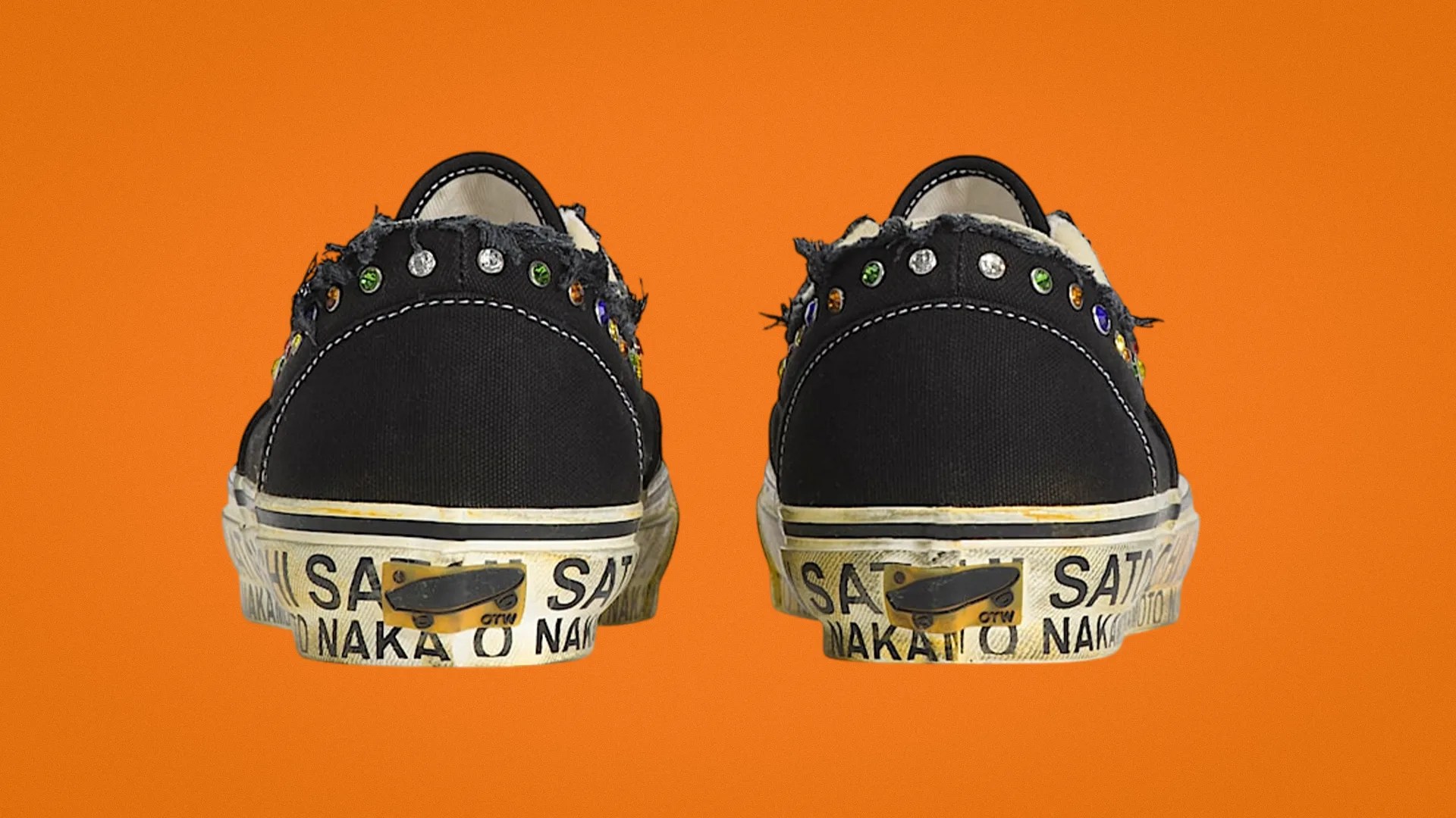 Pair of black canvas sneakers with frayed edges and multicolored rhinestones on the heel, on an orange background.