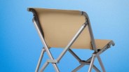 Foldable chair with beige fabric seat and backrest on a silver metal frame against a blue background.
