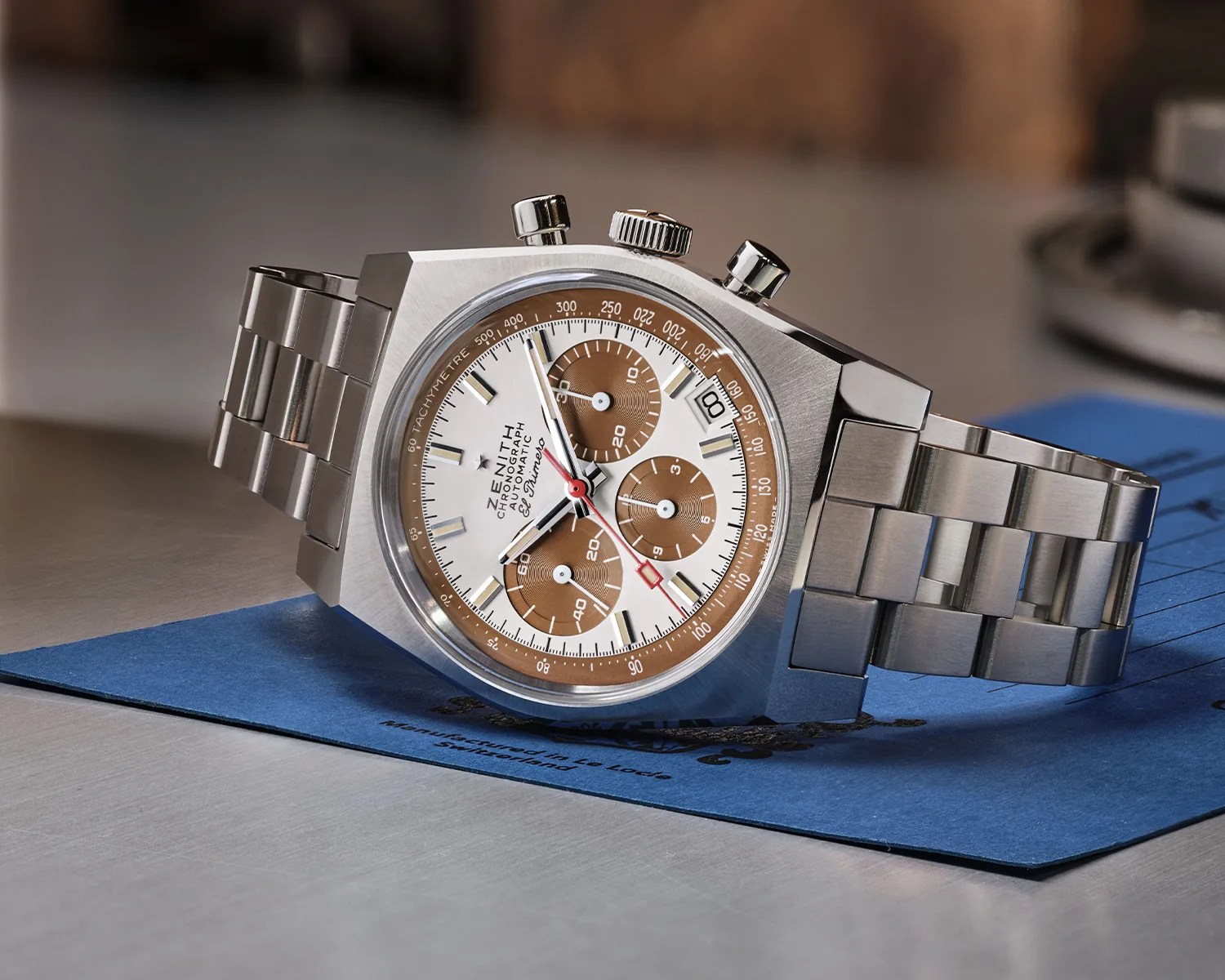 Stainless steel Zenith El Primero chronograph watch with white dial and brown subdials on a metal bracelet.