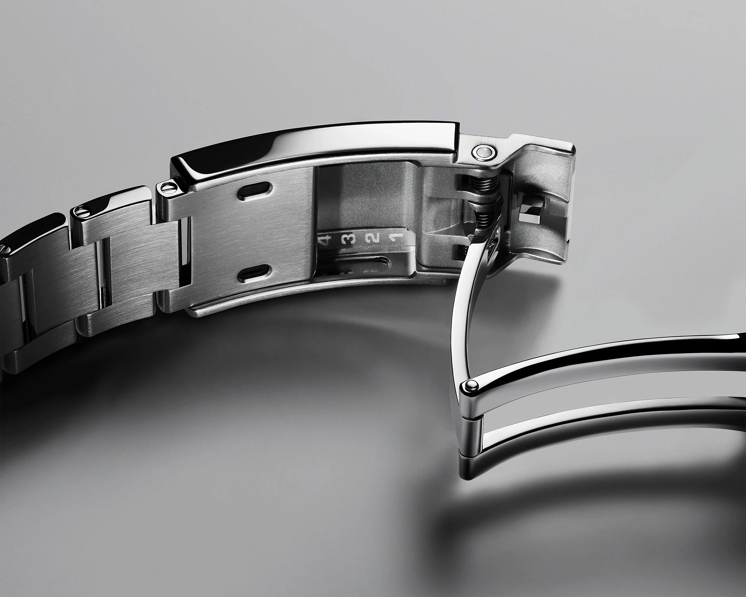 Close-up of a stainless steel watch bracelet with a partially open deployment clasp on a gray surface.