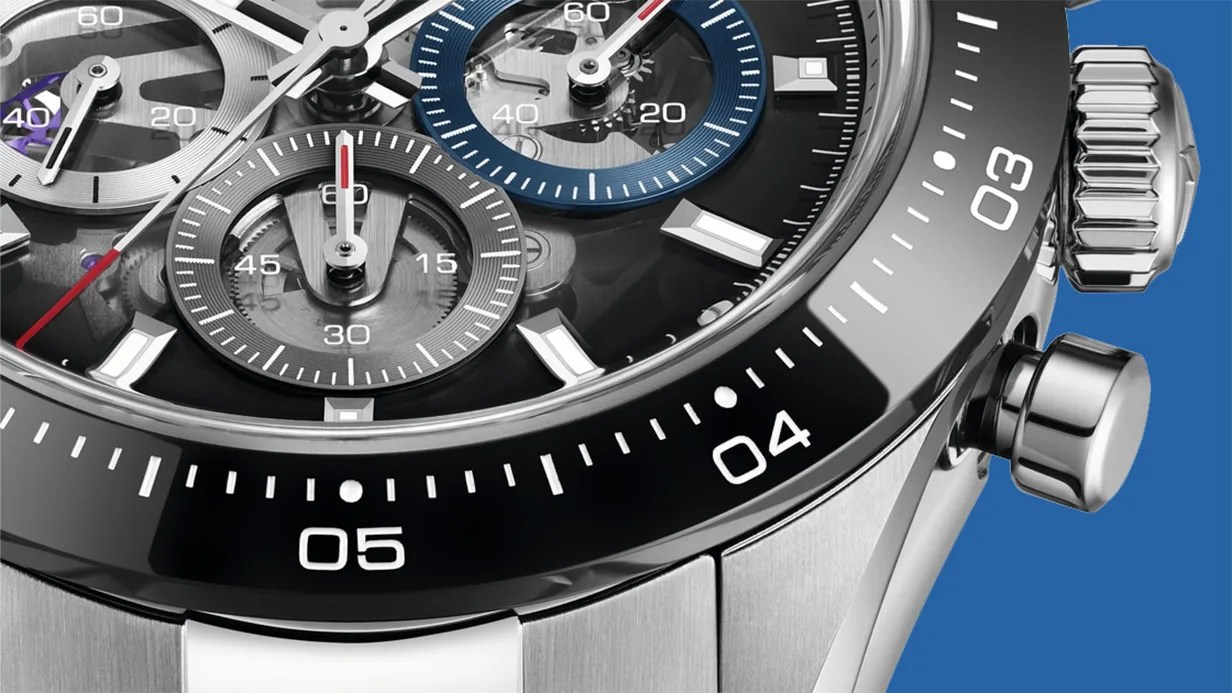 Close-up of a silver chronograph watch with black and blue subdials and a black bezel showing minute markers.