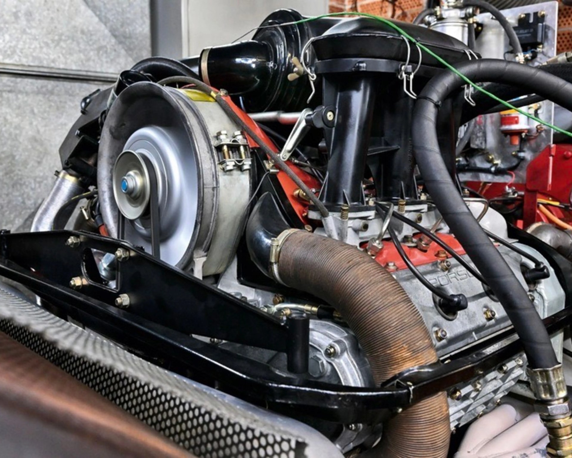 Close-up of a Porsche air-cooled engine with visible fan, black air intake, and large corrugated hose.