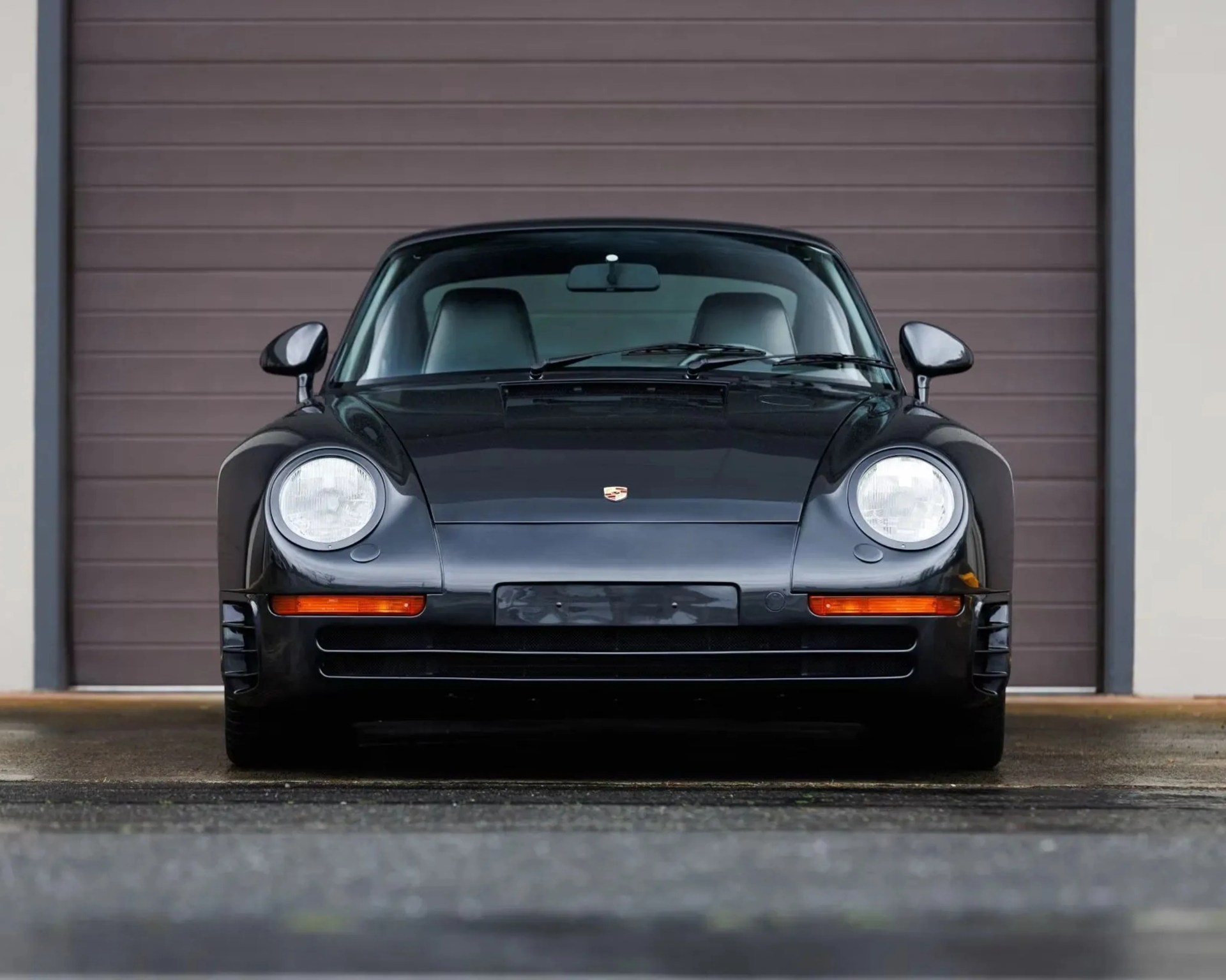 Front view of a black Porsche sports car parked in front of a closed brown garage door.