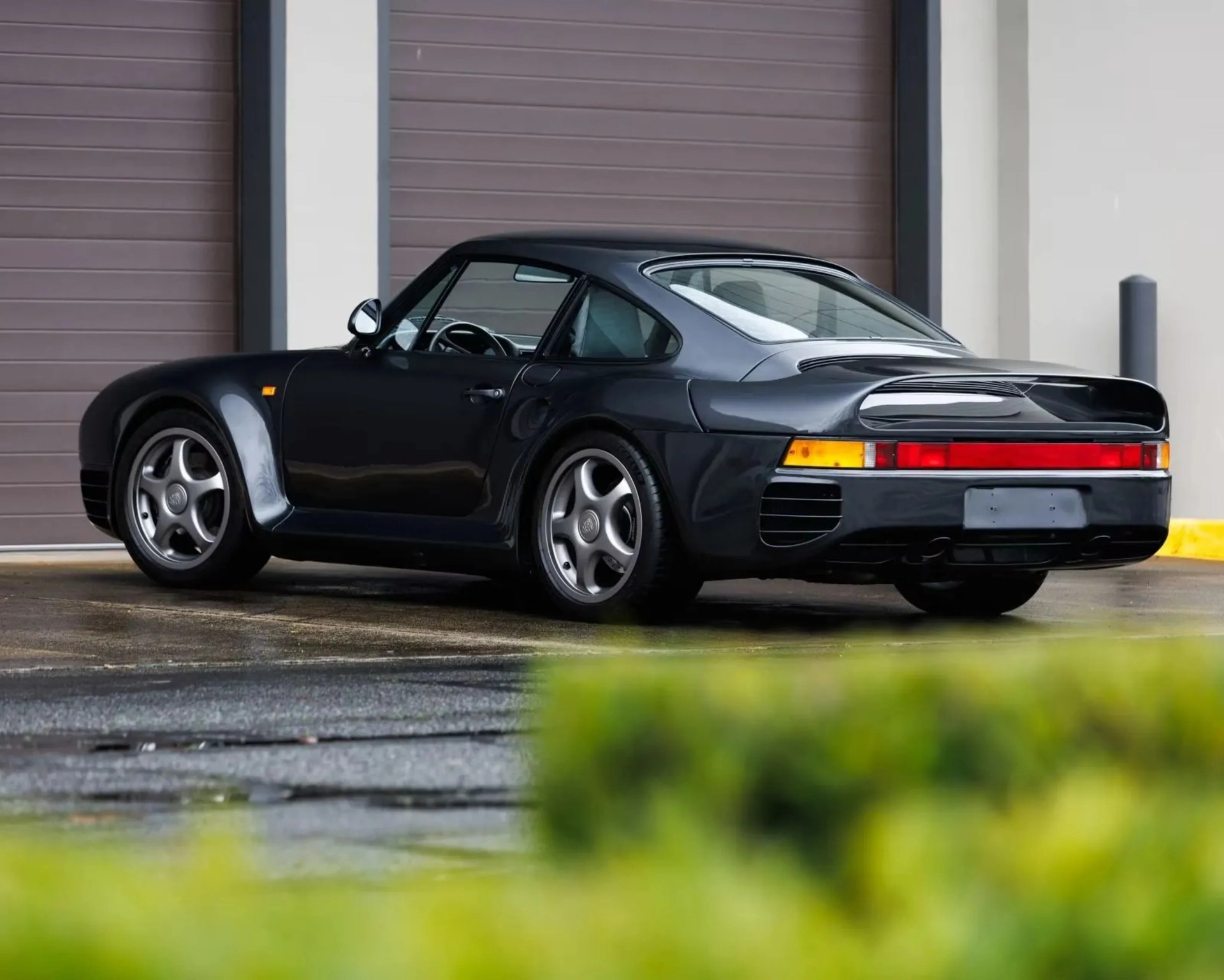 Black Porsche 959 sports car parked in front of a closed garage door.