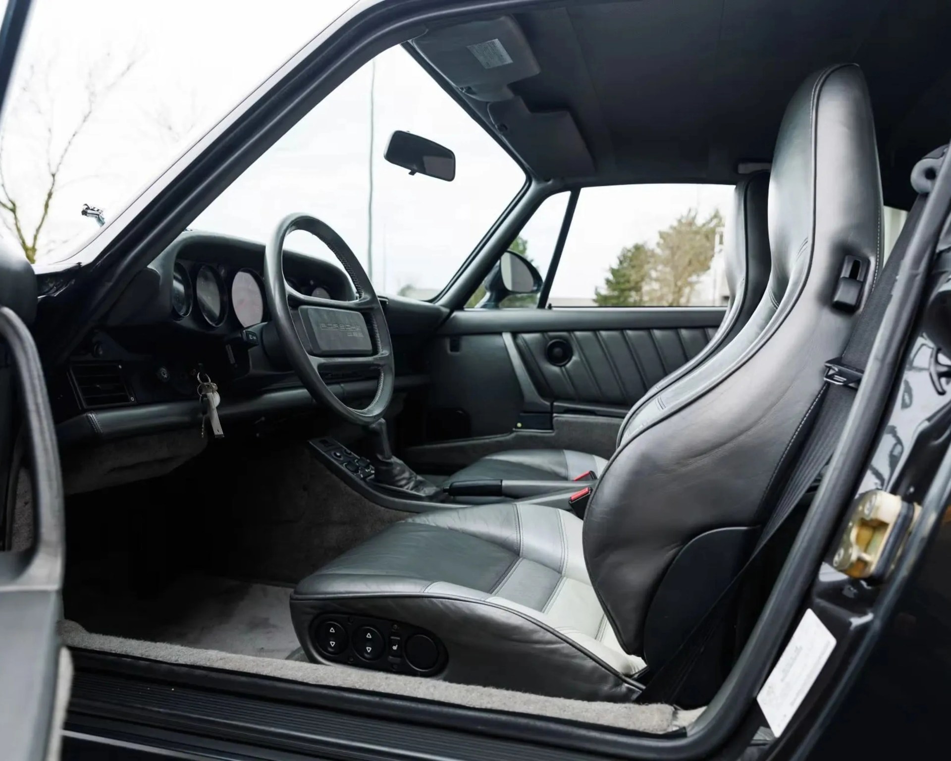 Black and gray leather bucket seats inside a classic car with a black steering wheel and dashboard.