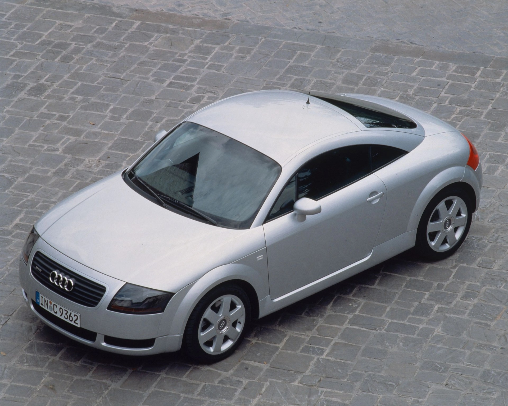 Silver Audi TT coupe parked on a cobblestone street, viewed from above.