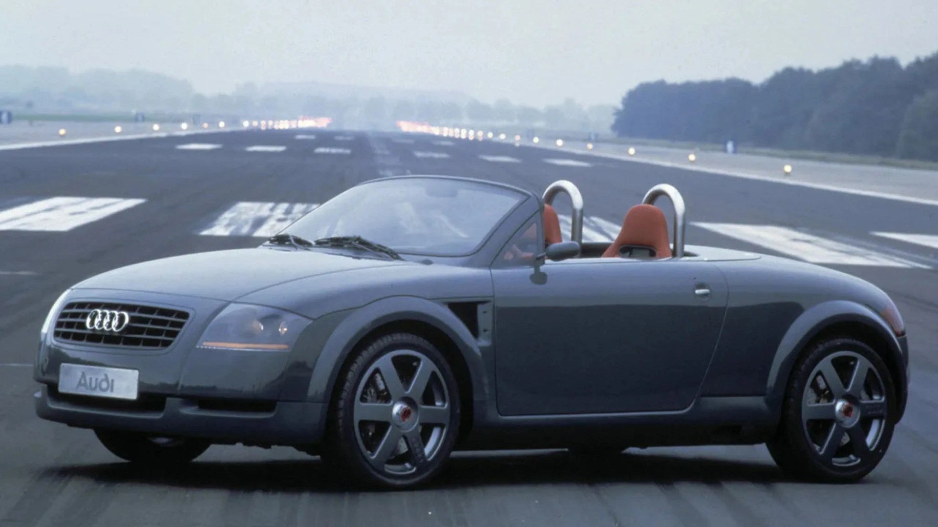 Dark gray Audi convertible sports car with red seats on an airport runway.