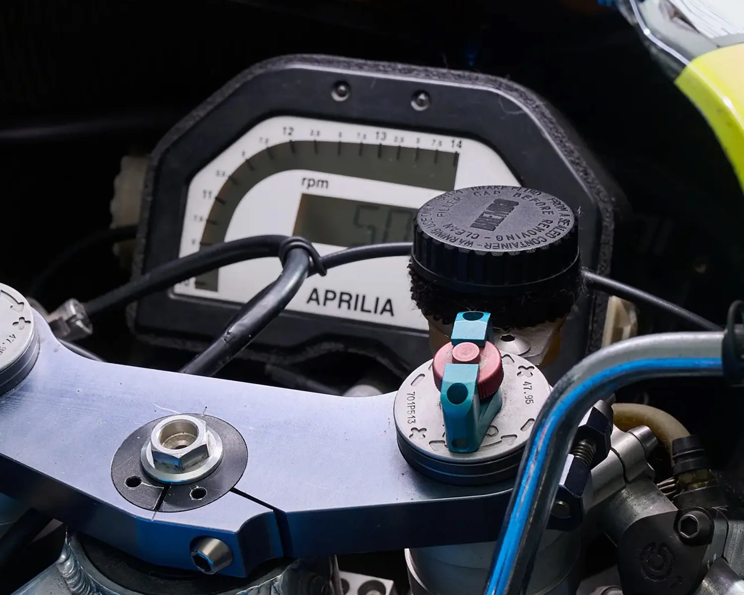 Close-up of Aprilia motorcycle dashboard showing rpm gauge and handlebar components with cables.