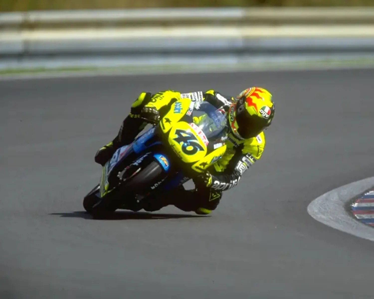 Motorcycle racer in yellow gear leaning into a turn on a racetrack.