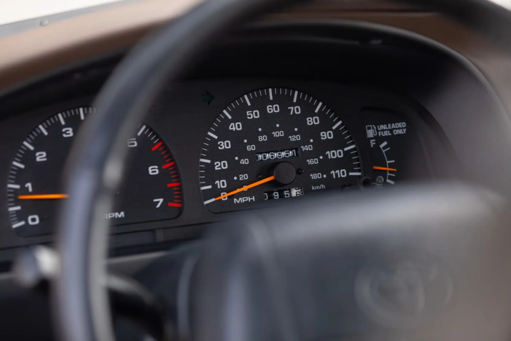 Car dashboard showing speedometer, tachometer, and fuel gauge behind a steering wheel.