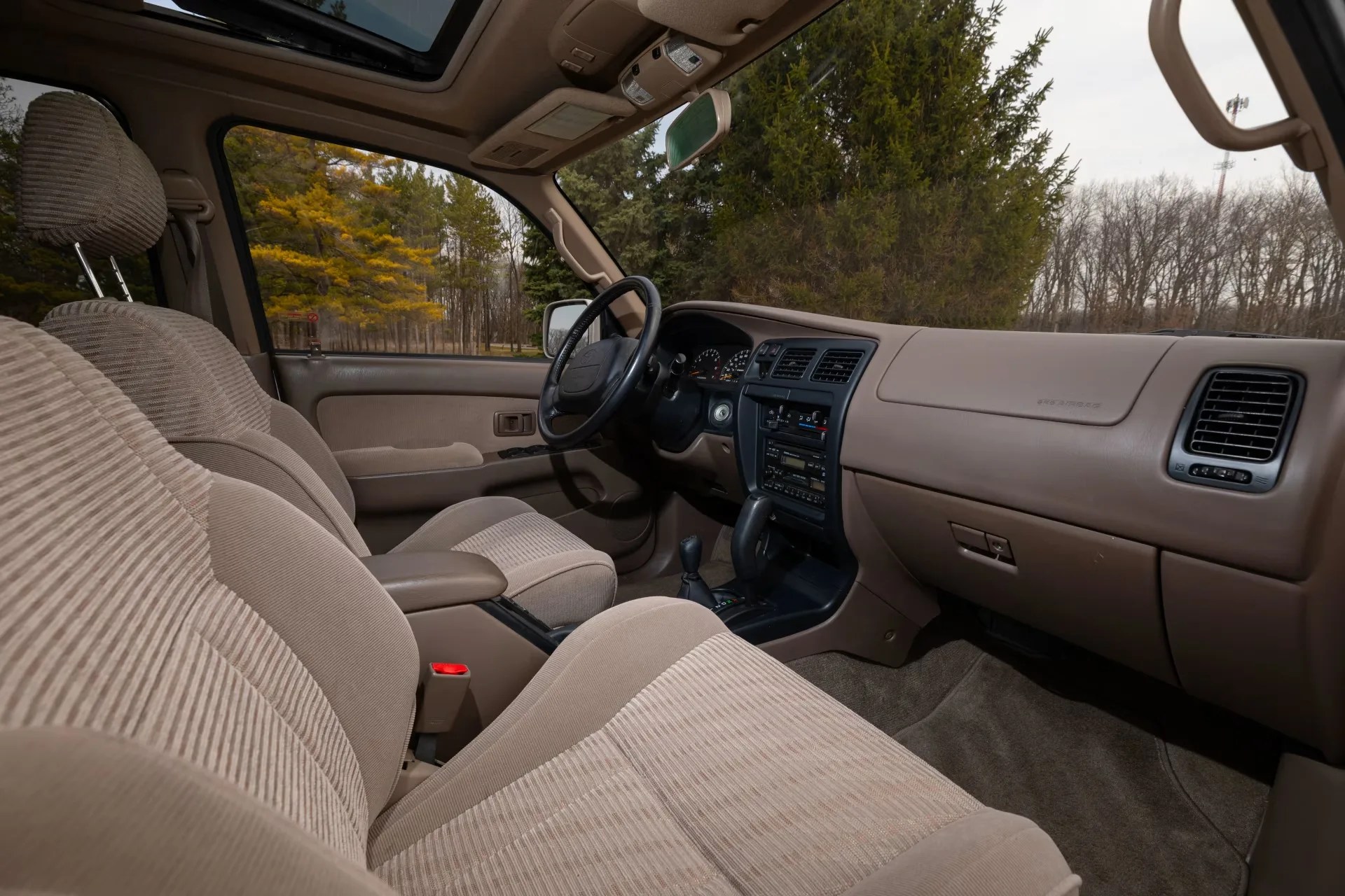 Beige cloth car interior with front seats, black steering wheel, and dashboard with air vents and controls.