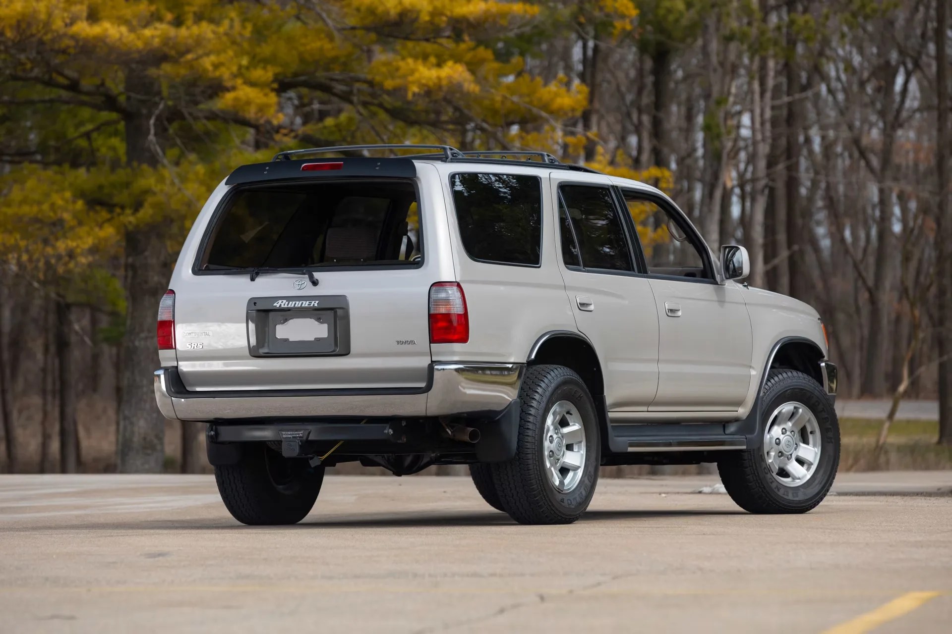 Silver Toyota 4Runner SR5 SUV parked on pavement with autumn trees in the background.
