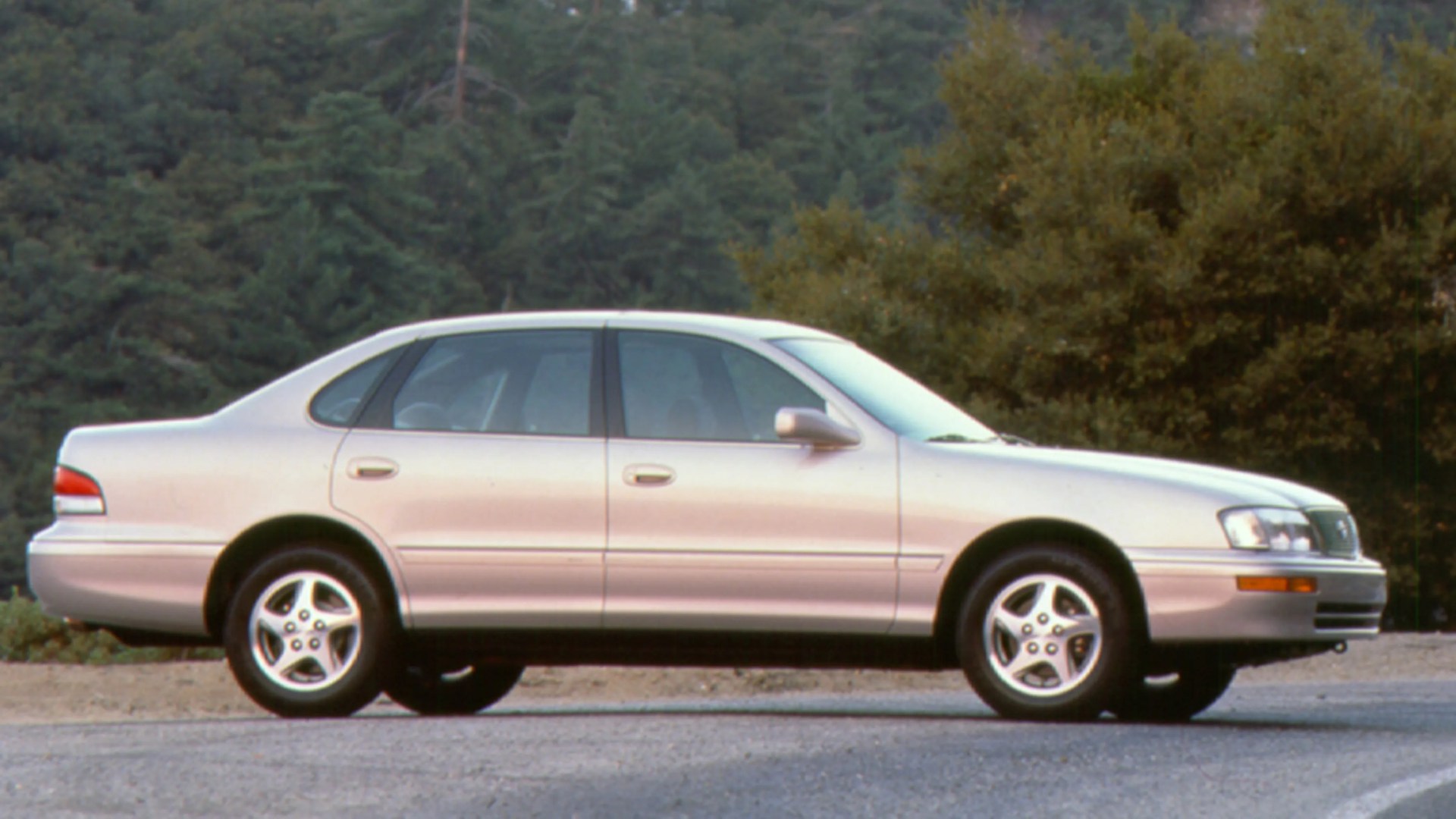 Silver four-door sedan parked on a gravel road with trees in the background.
