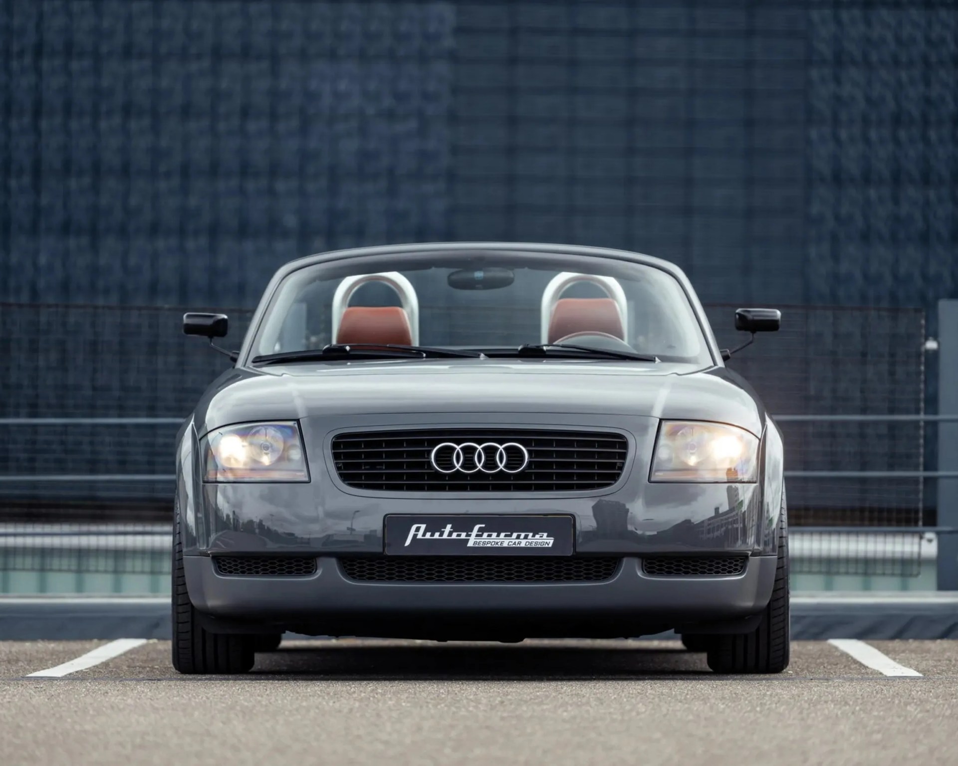 Front view of a gray Audi convertible with red seats and a black grille parked in a lot.
