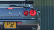 Rear view of a dark gray Nissan Skyline GT-R M-spec with round taillights and a yellow UK license plate.