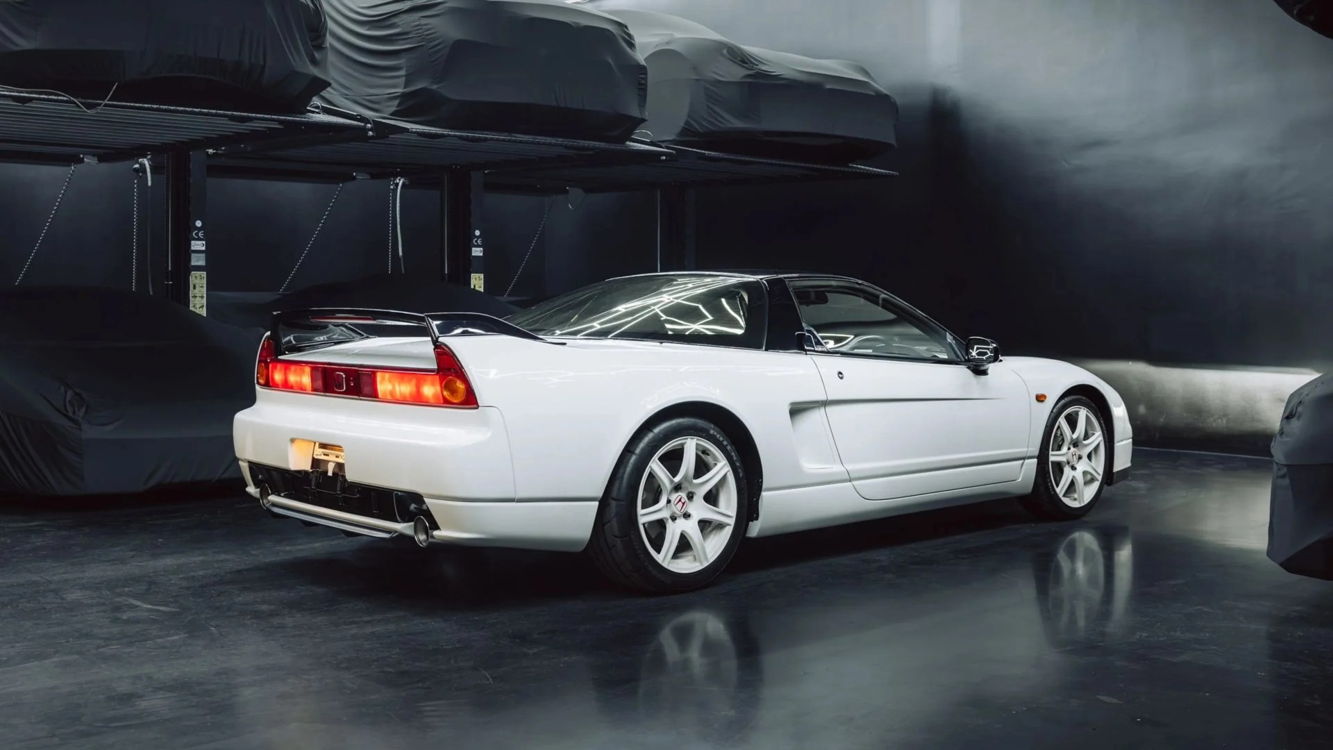 White Honda NSX sports car with black roof and rear spoiler in a dark garage.