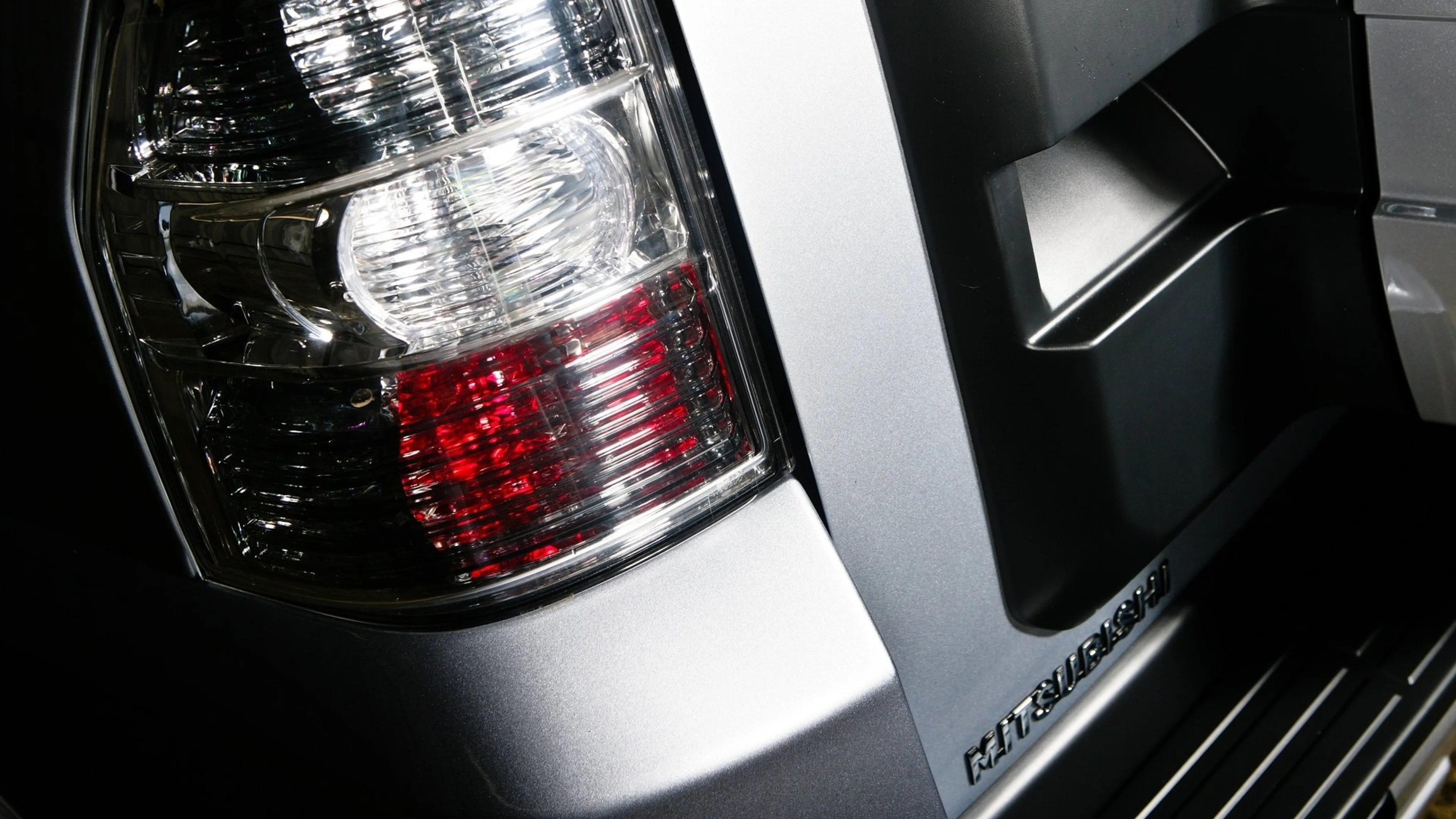 Close-up of a silver Mitsubishi vehicle's rear tail light and part of the rear bumper with the Mitsubishi logo.