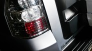 Close-up of a silver Mitsubishi vehicle's rear tail light and part of the rear bumper with the Mitsubishi logo.