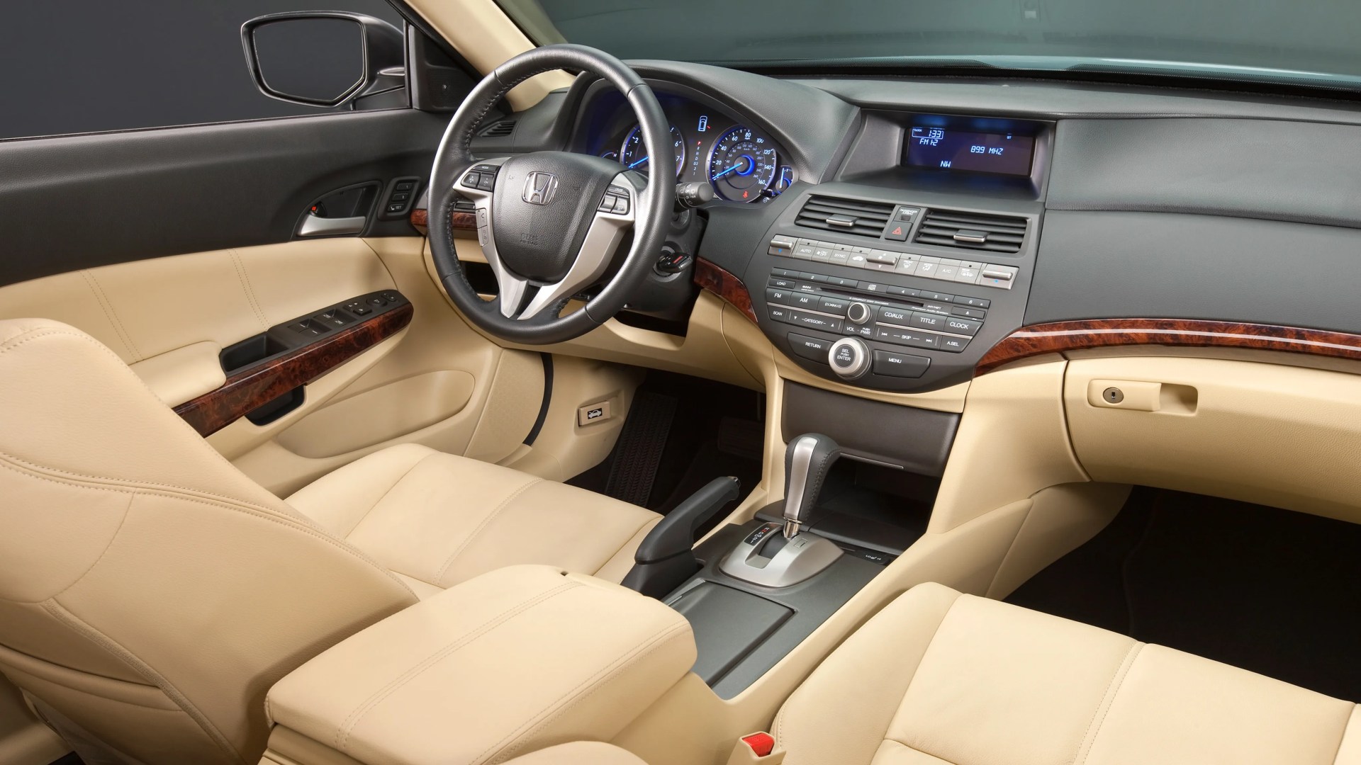 Beige leather car interior with black and wood trim, black steering wheel with Honda logo, and center console with gear shift.