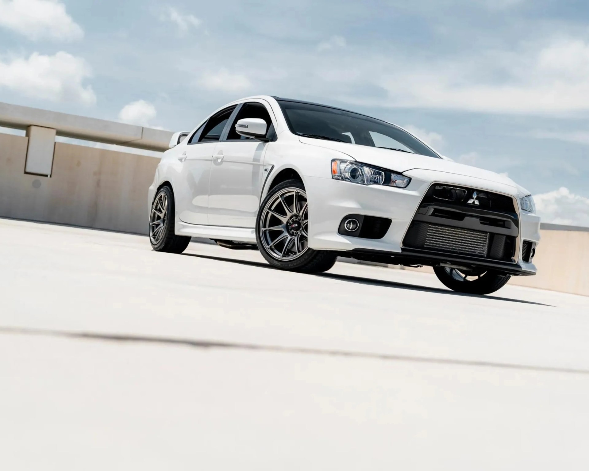 White Mitsubishi Lancer Evolution with black grille and aftermarket wheels on a rooftop parking lot.