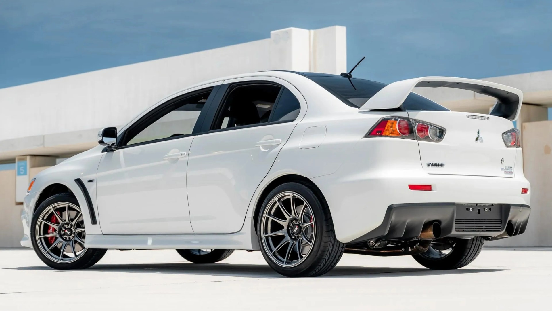 White Mitsubishi Lancer Evolution with black roof, rear spoiler, and multi-spoke alloy wheels parked outdoors.