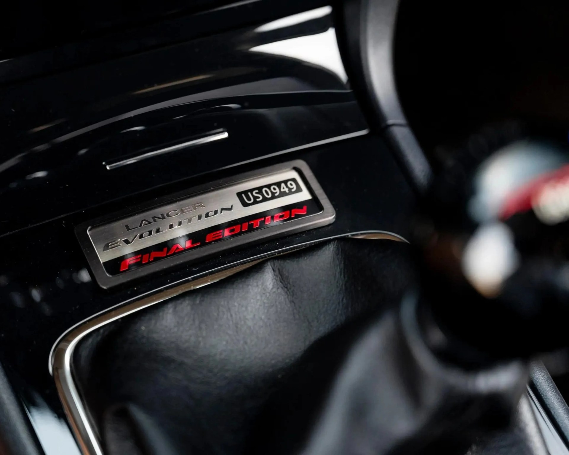 Metal badge with "Lancer Evolution Final Edition US0949" on a black glossy car interior panel.