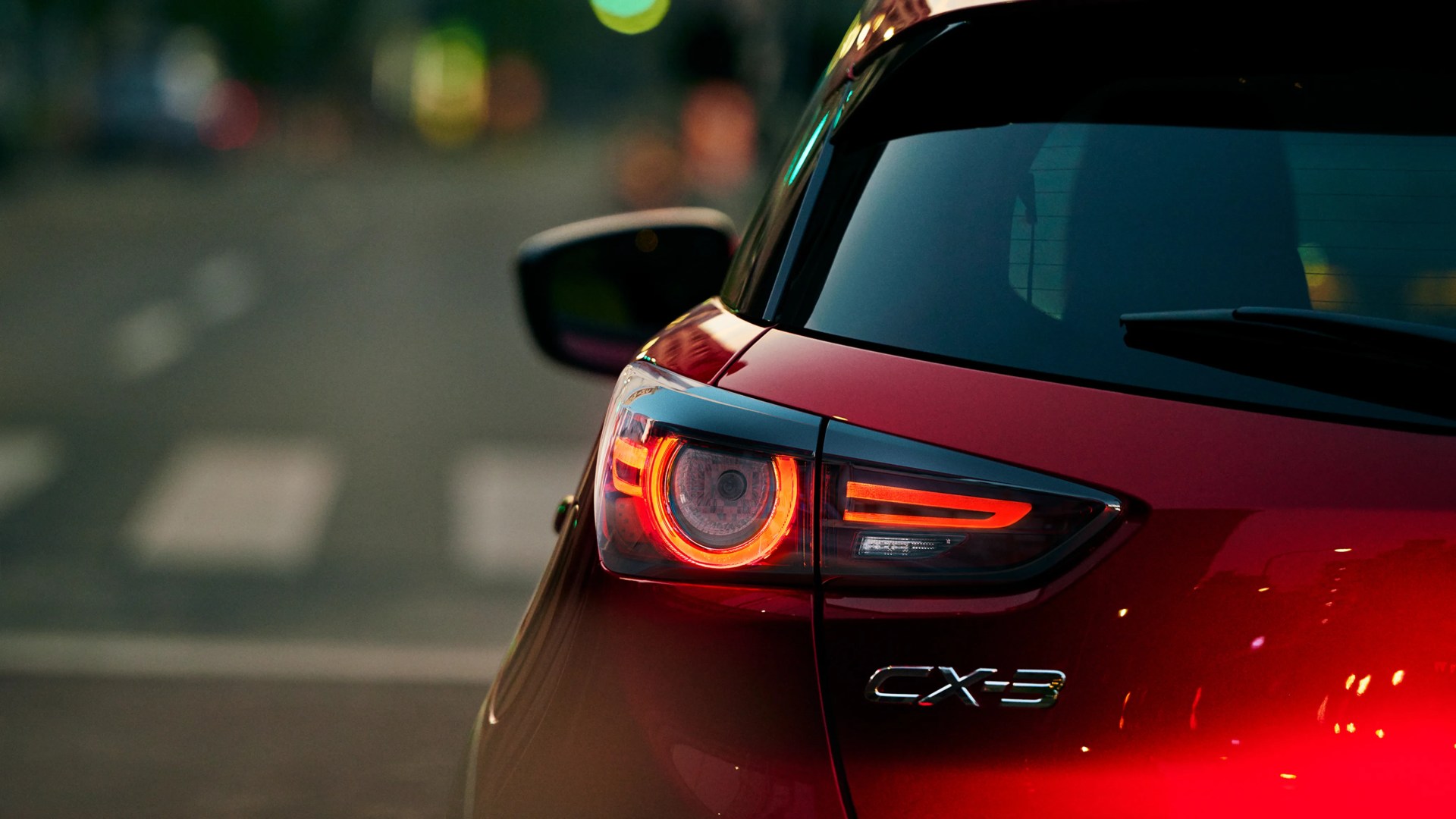 Rear view of a red Mazda CX-3 with illuminated taillight and rear windshield wiper.