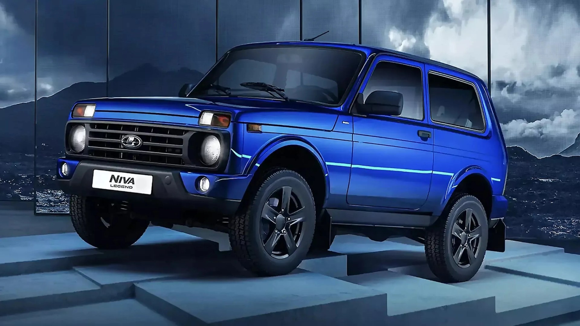 Blue Lada Niva Legend SUV with black wheels on a stepped platform against a mountainous backdrop.