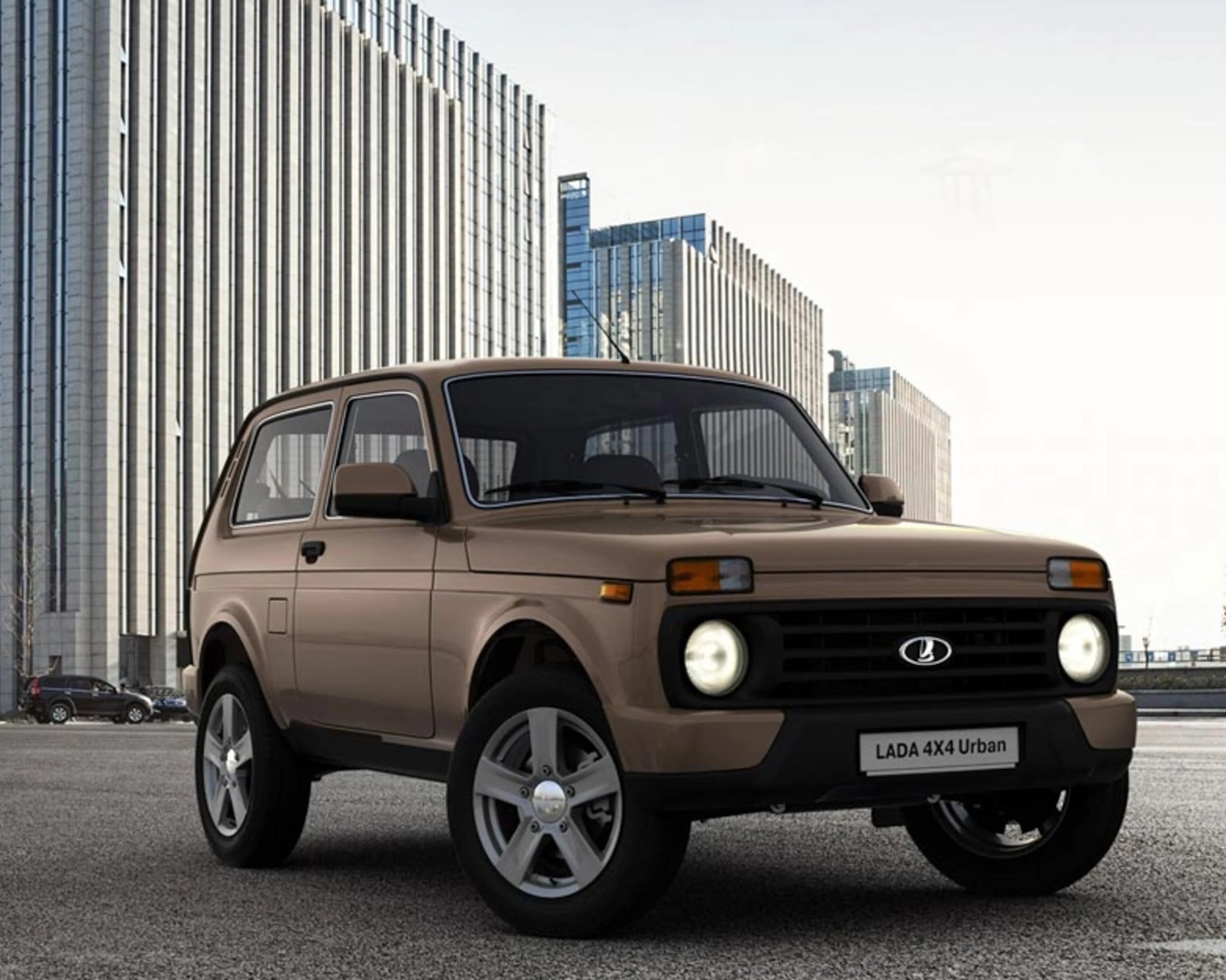 Brown LADA 4x4 Urban SUV with round headlights parked on asphalt in front of tall modern buildings.
