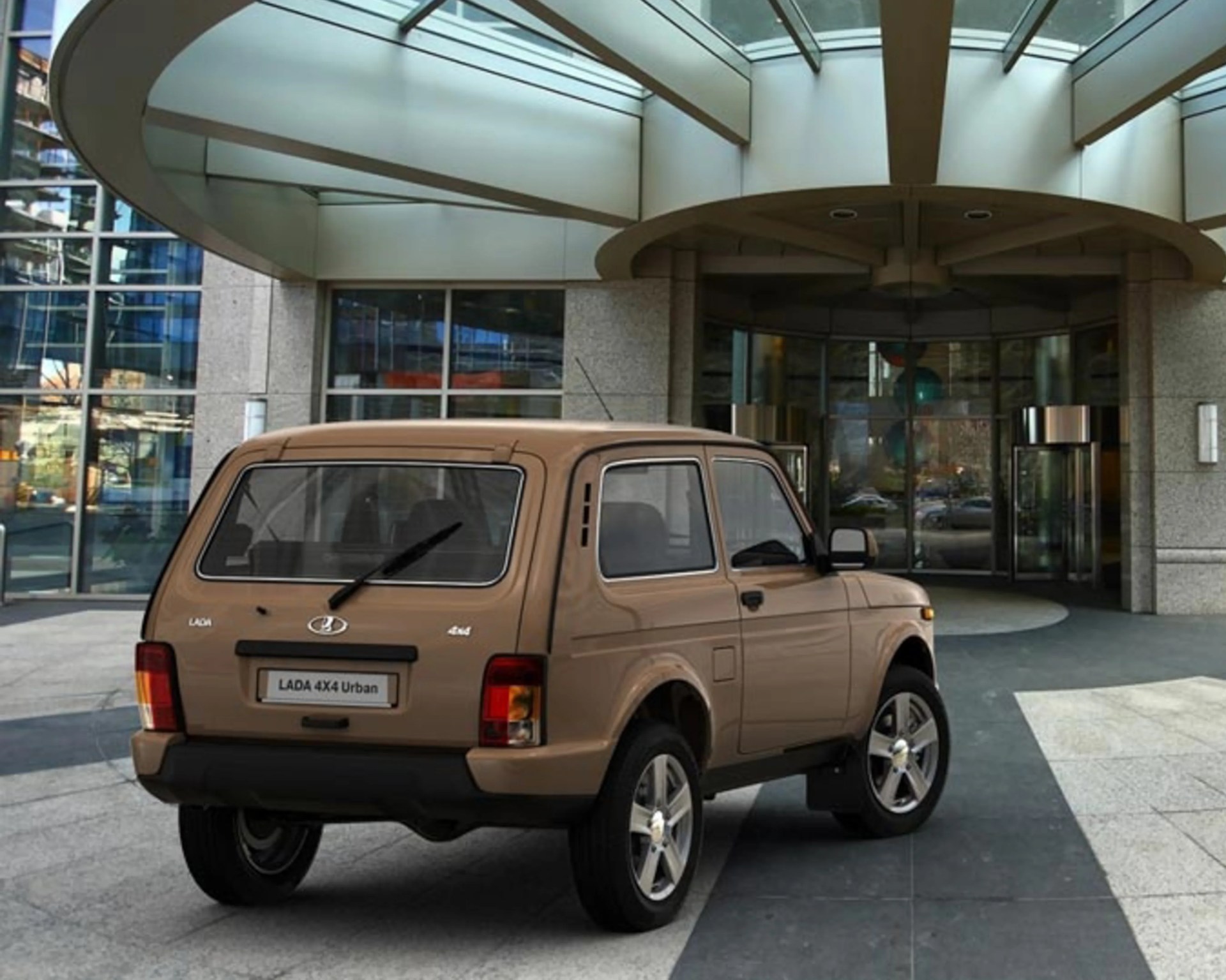 Beige LADA 4x4 Urban SUV parked under a modern glass and concrete building entrance.