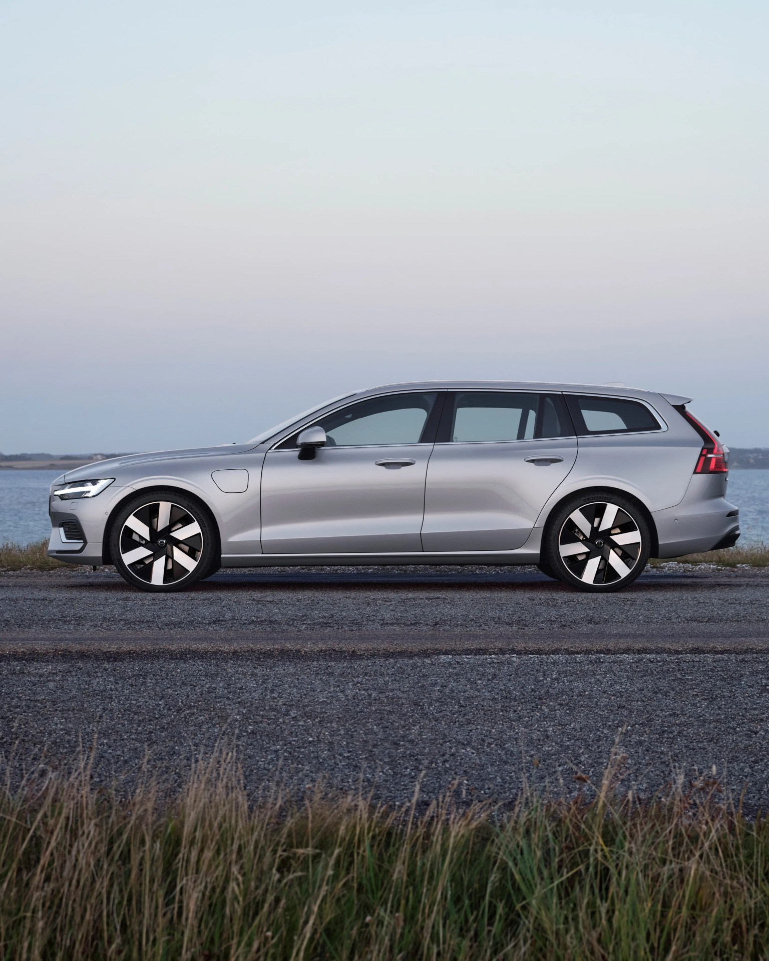 Silver electric station wagon parked on a gravel road near water at dusk.