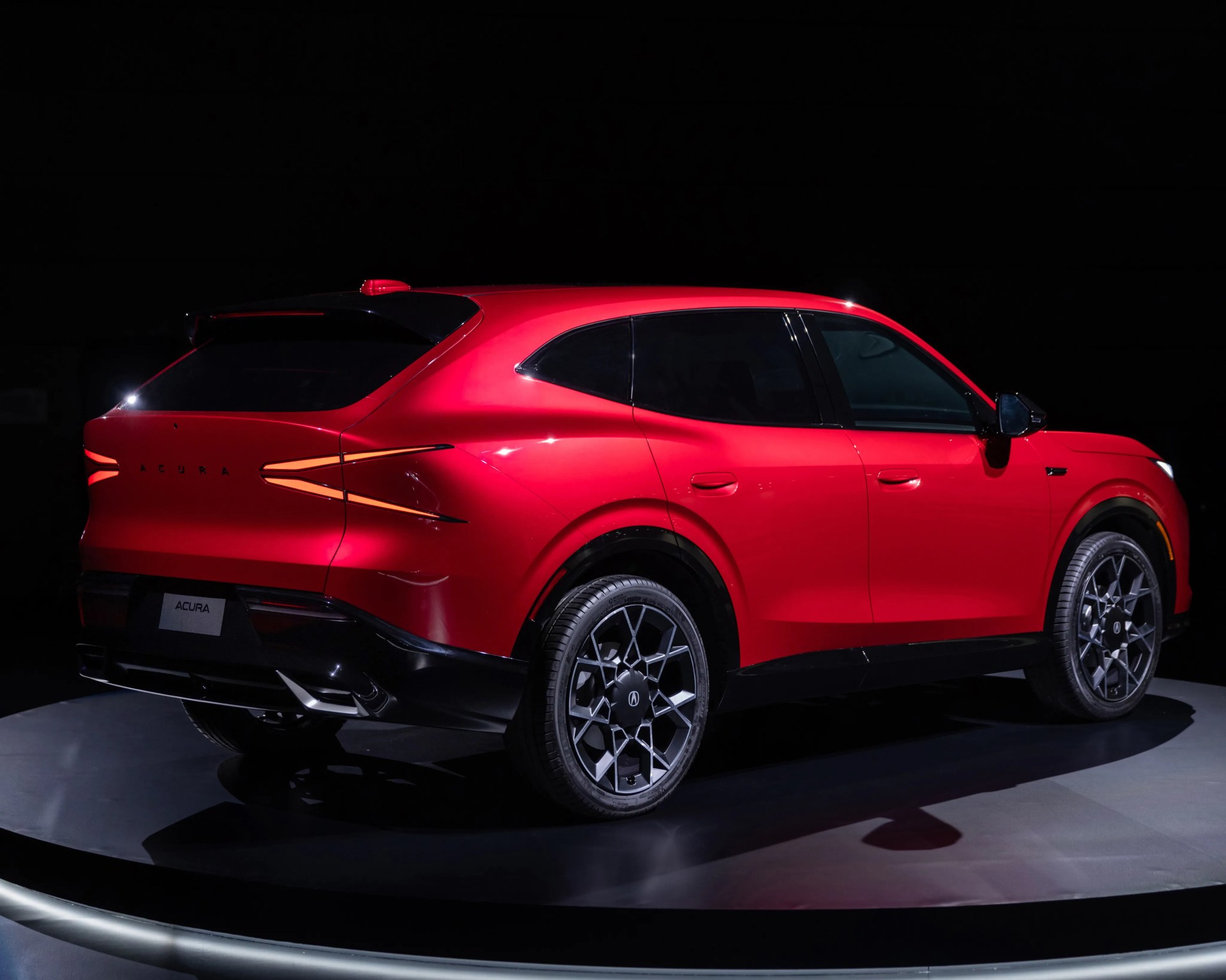 Red Acura SUV with black roof and dark alloy wheels shown from rear side on a dark background.