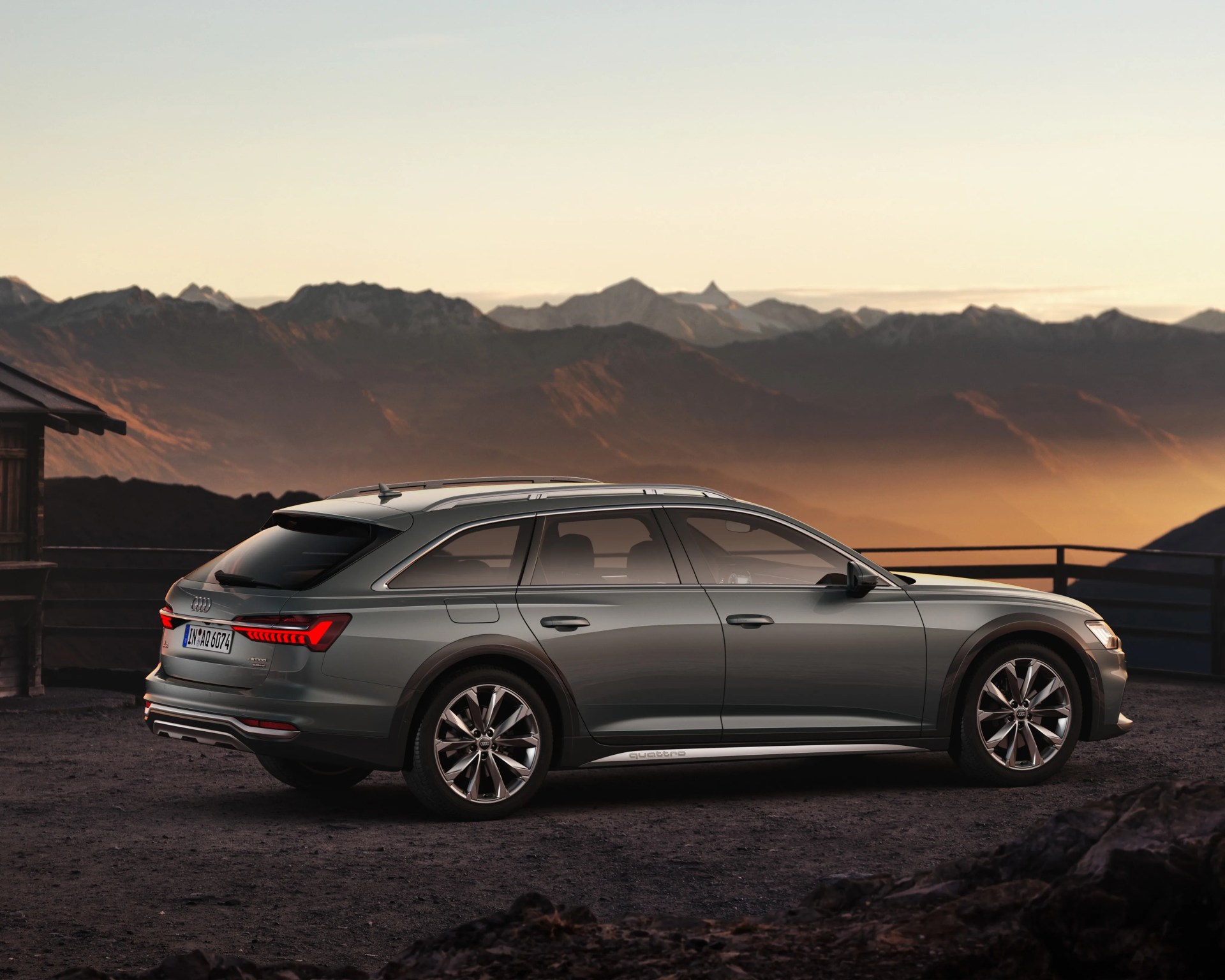 Gray Audi allroad quattro wagon parked on a gravel surface with mountains in the background at sunset.