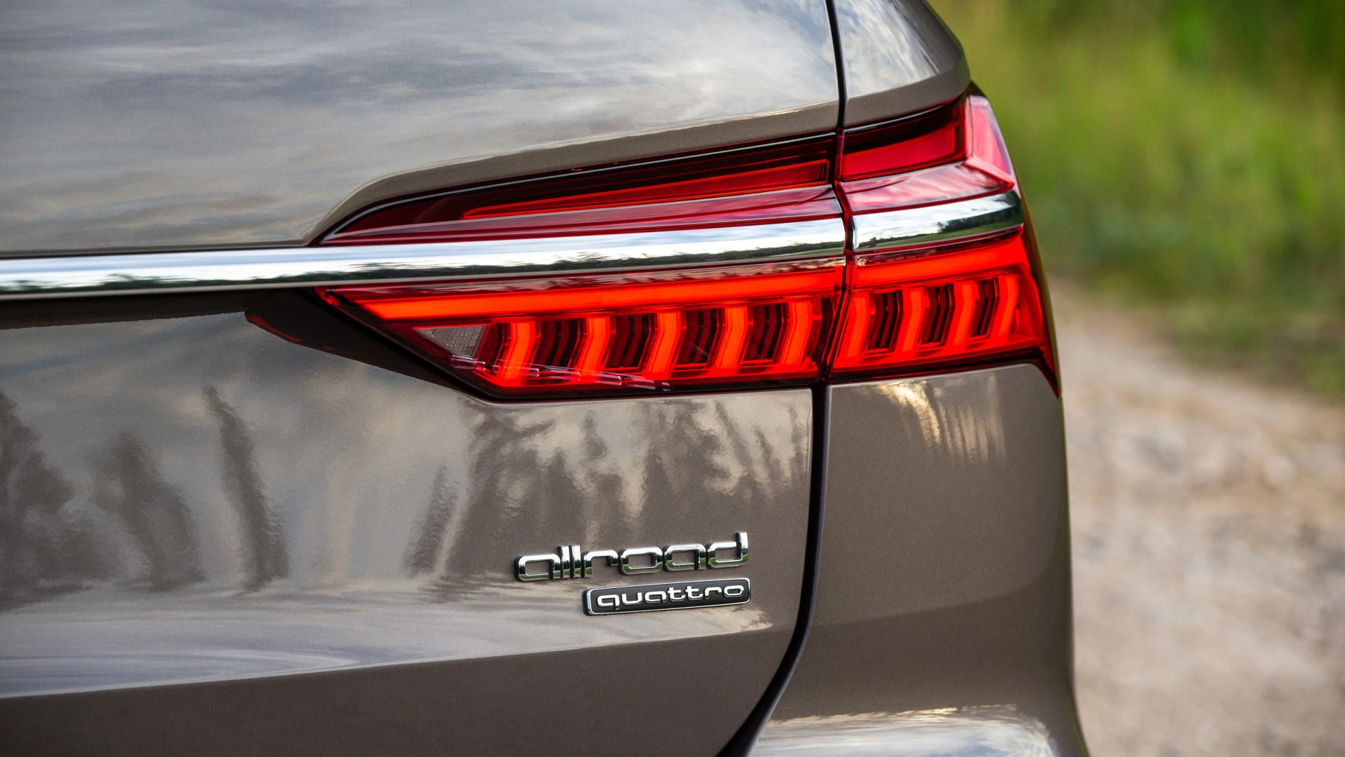 Close-up of a gray car's rear with illuminated red taillight and "allroad quattro" badges.