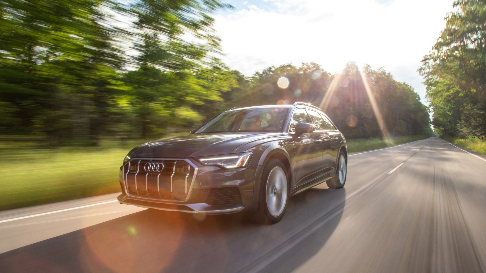 Black Audi SUV driving on a sunlit road with blurred green trees in the background.