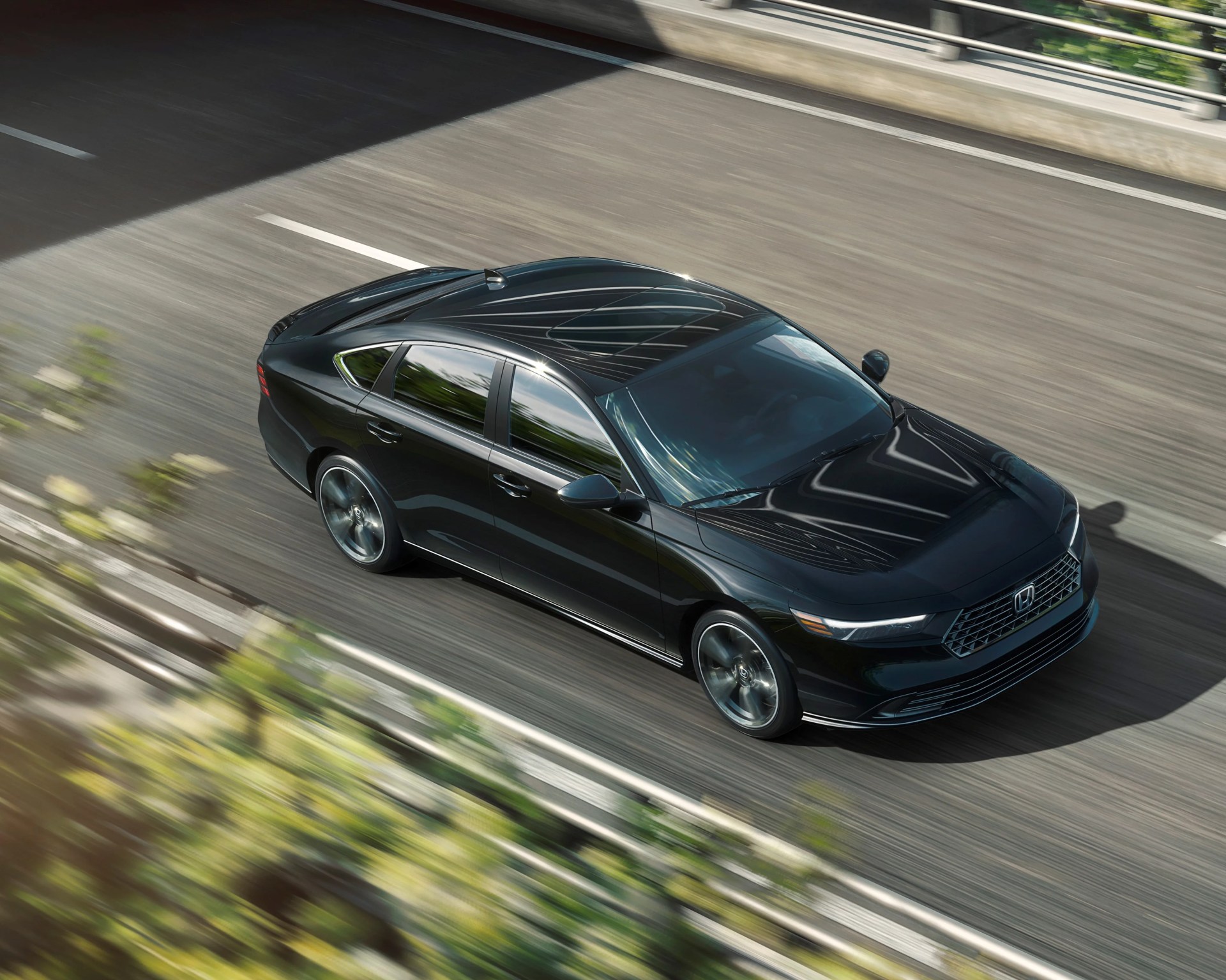 Black Honda sedan driving on a sunlit highway with reflections on the windows and roof.