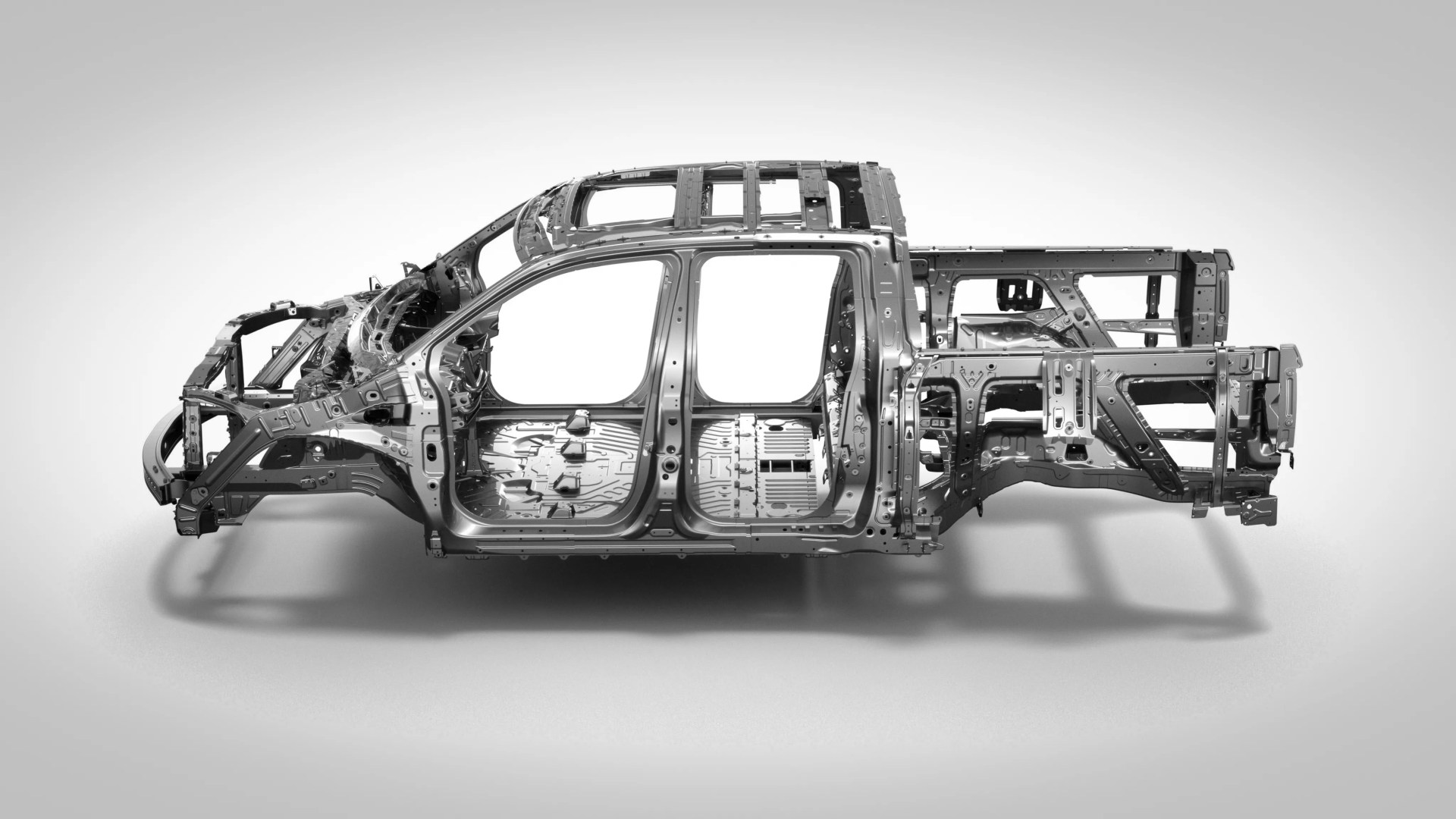 Exposed silver metal frame of a pickup truck body without panels or wheels on a gray background.