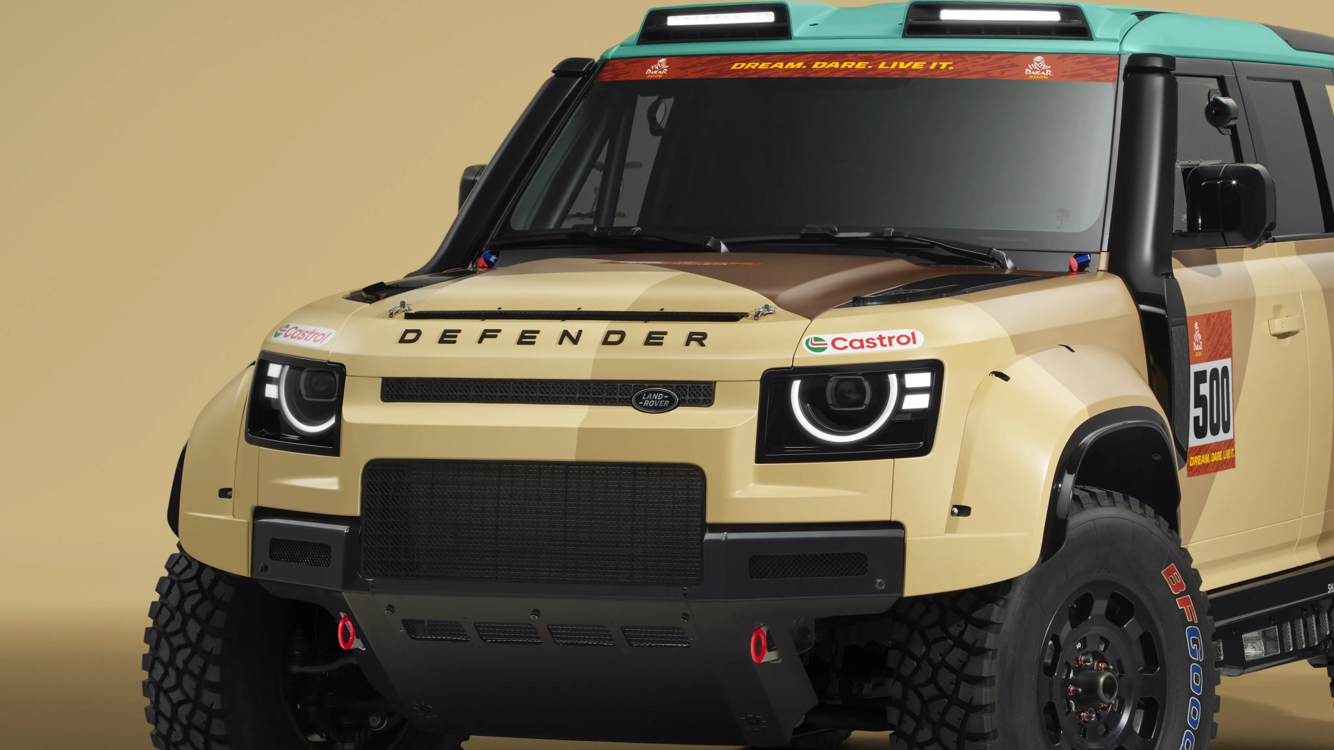Front view of a beige Land Rover Defender Dakar rally edition with black accents and large off-road tires.