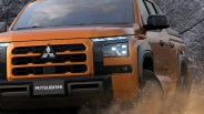 Orange Mitsubishi pickup truck front with black grille and headlights kicking up dust.