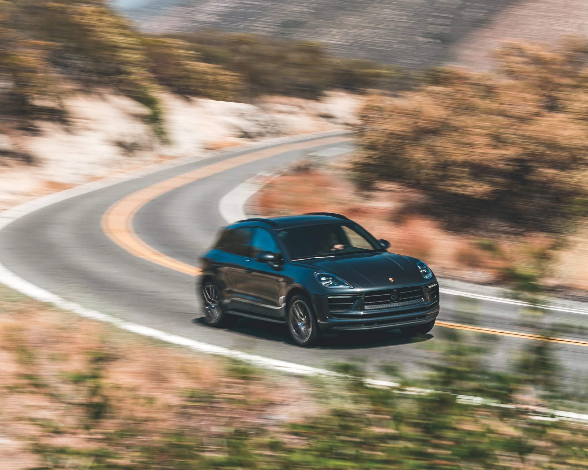 Black Porsche SUV driving on a winding mountain road with blurred background.