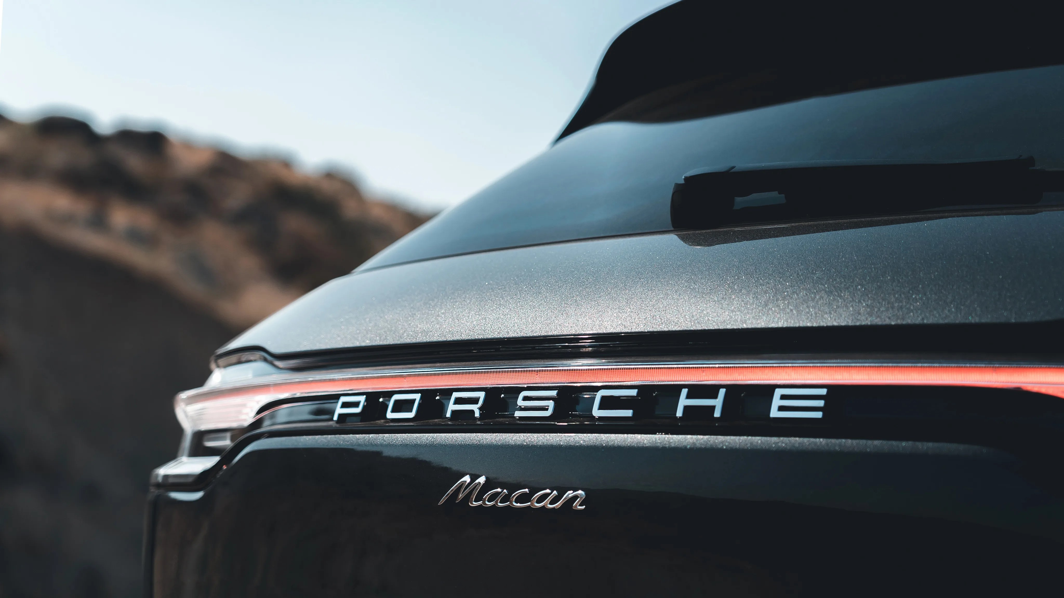 Rear view of a black Porsche Macan with visible Porsche logo and rear windshield wiper.