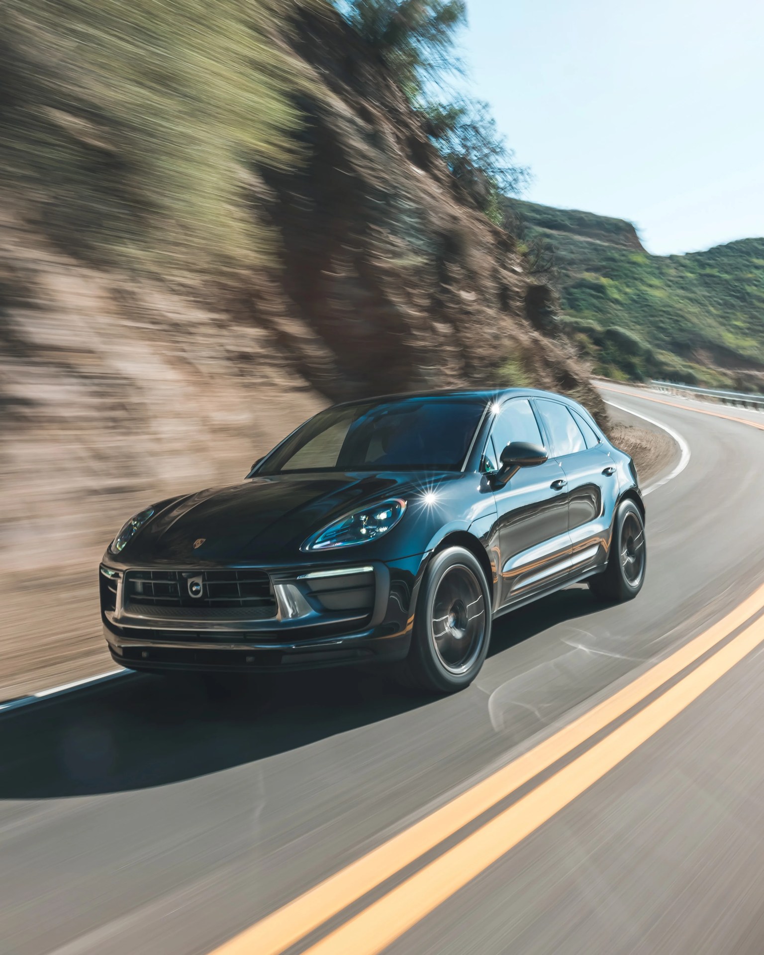 Black Porsche SUV driving on a winding mountain road with blurred background.