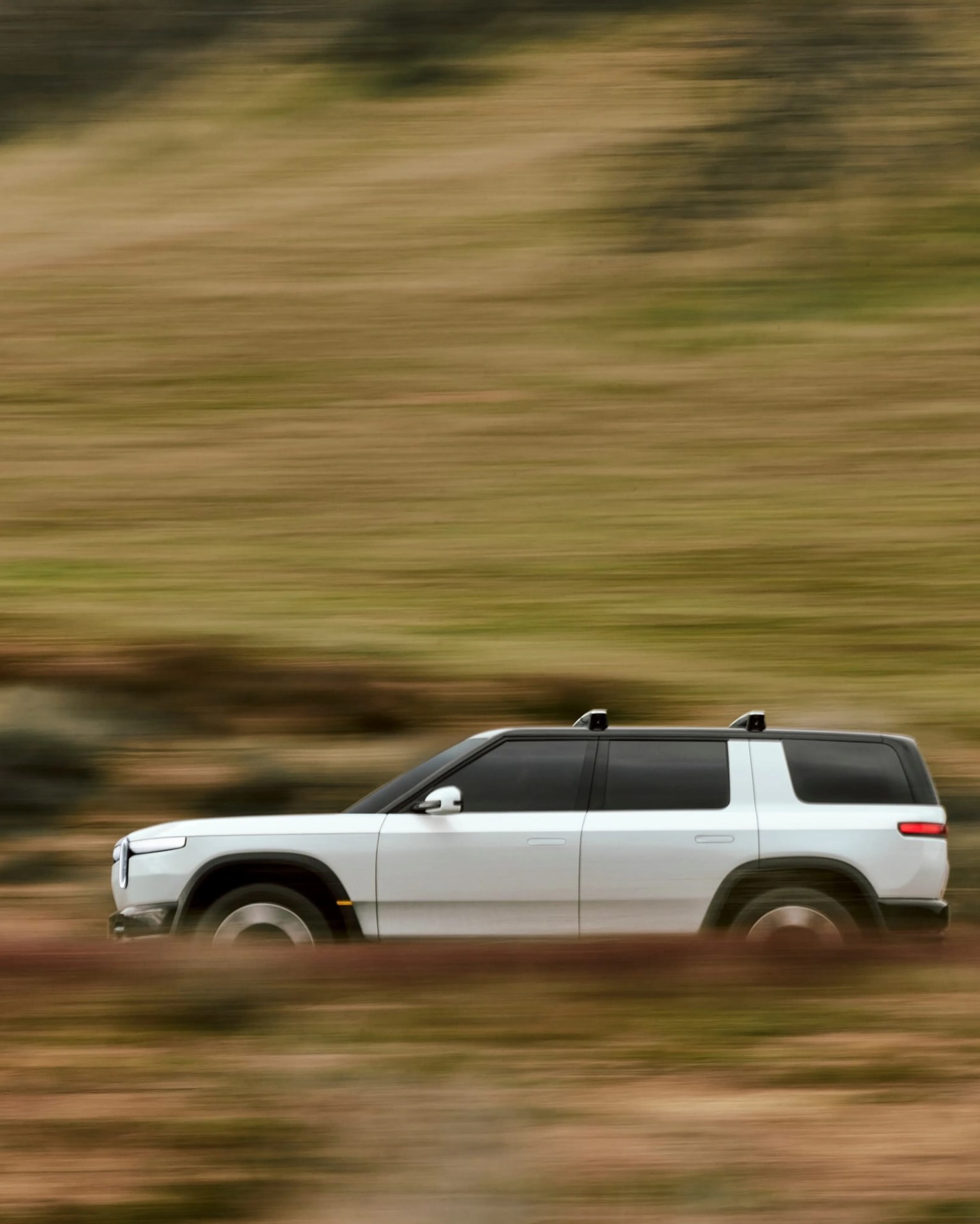 White SUV with black roof and tinted windows driving fast on a blurred grassy landscape.