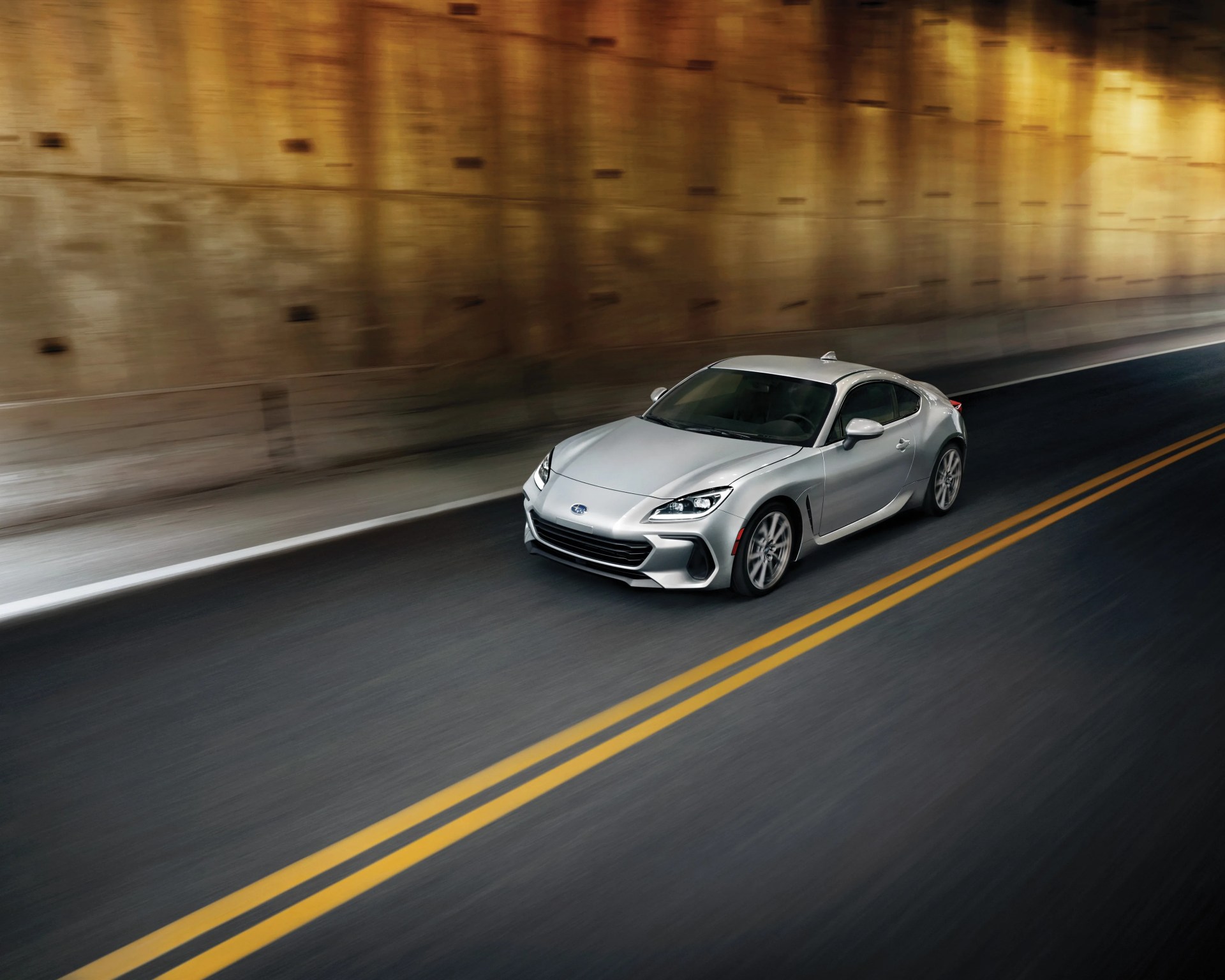Silver Subaru sports car driving in a tunnel with yellow double lines on the road.