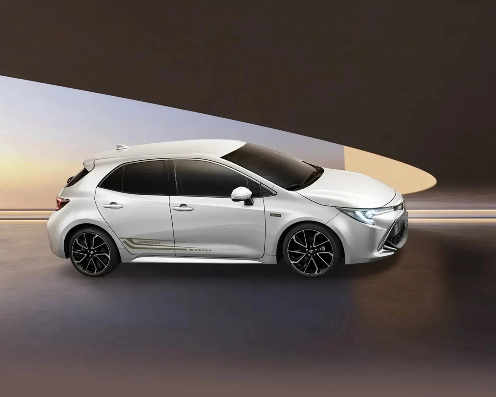 White Toyota Corolla hatchback with black alloy wheels and tinted windows in a modern setting.